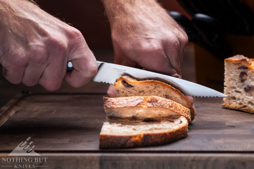 A close-up of the Calphalon Classic serrated utility knife being used to slice a loaf of bread on top of a wood cutting board. 