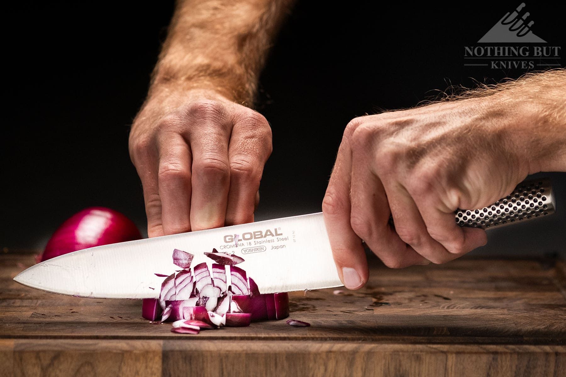 A Global G2 chef knife being held in a pinch grip dicing a red onion.
