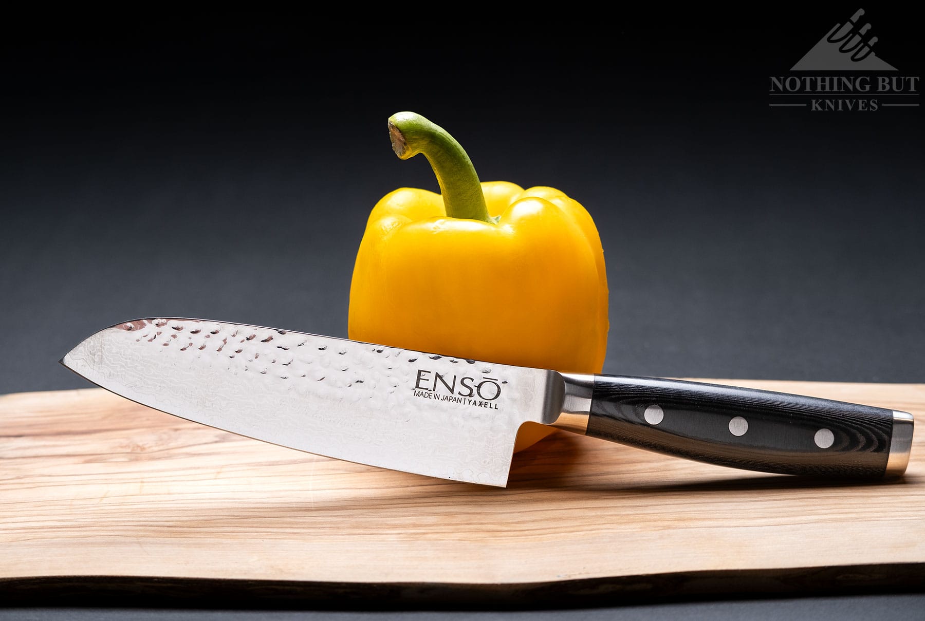 The Enso HD santoku knife leaning against a yellow bell pepper on a wood cutting board.