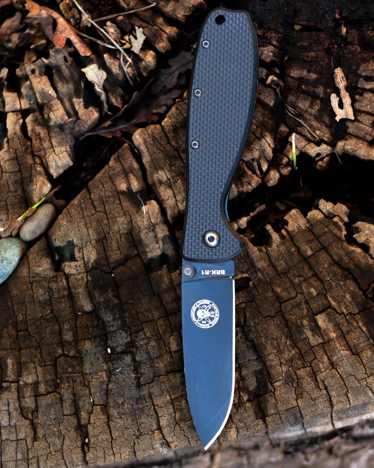 A black Esee Zancudo pocket knife with its blade open sitting on a tree stump.