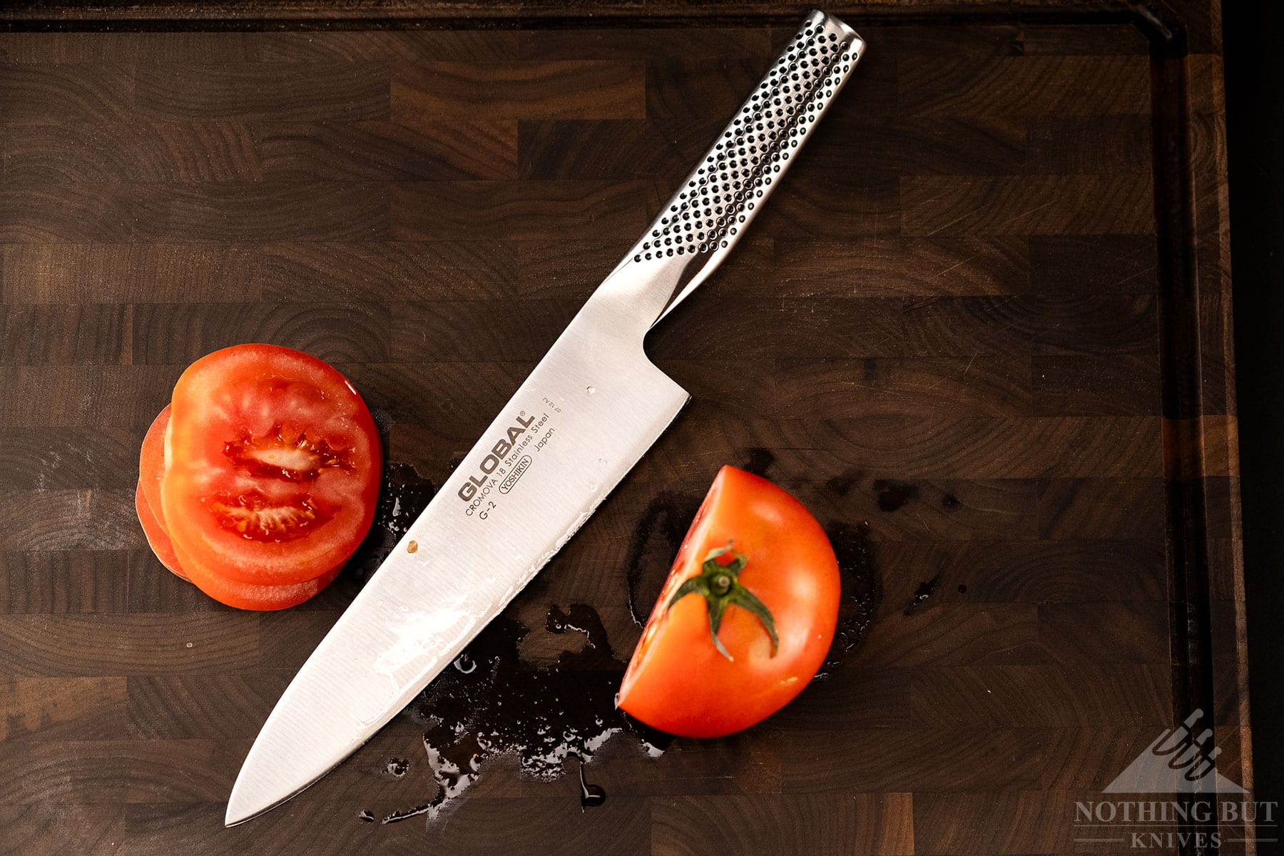 An overhead view of the 8-inch Global Japanese chef in-between two sides of a tomato it just sliced in half.