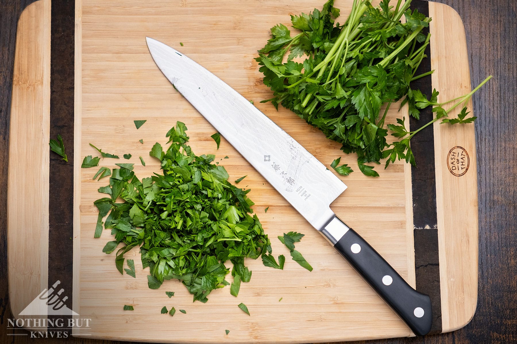 An Overhead view of the 8-inch Tojiro DP Damascus chef knife on a bamboo cutting board between to piles of herbs it was used to dice. 