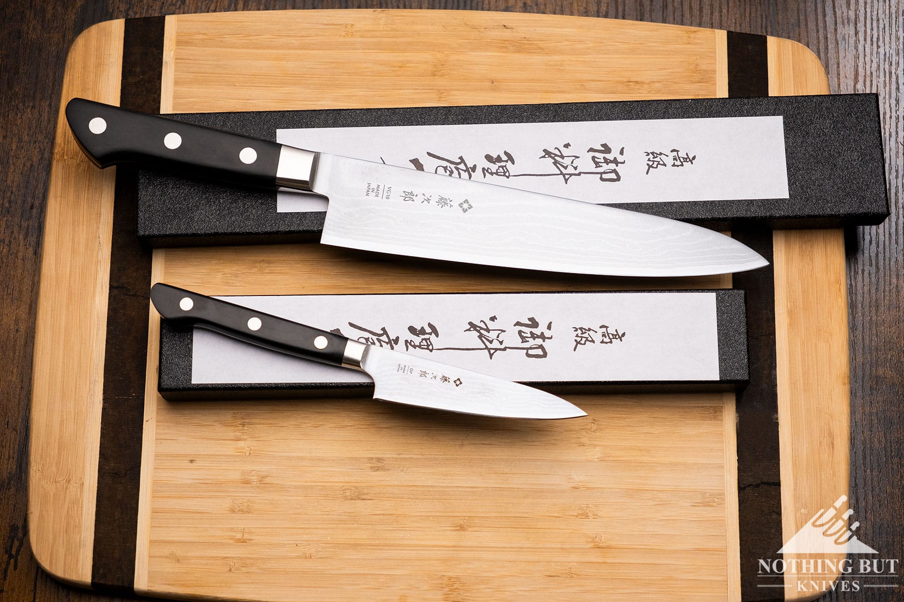 An overhead view of the Tojiro DP Damascus chef knife and paring knife on top of their boxes on a Bamboo cutting board. 