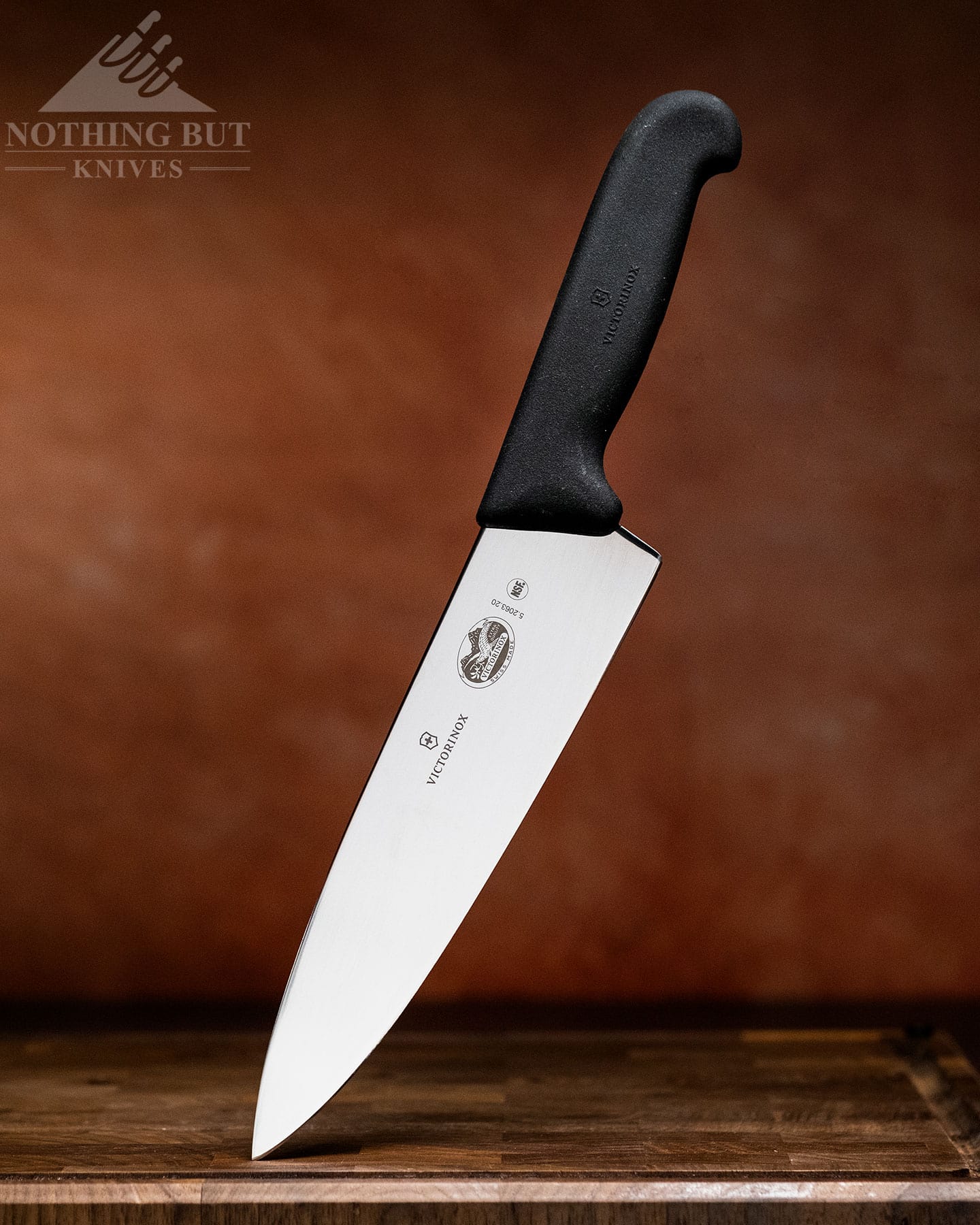 A profile shot Victorinox Fibrox 8-inch chef knife with its blade tip facing down on a cutting board and its handle pointed towards the top left corner.