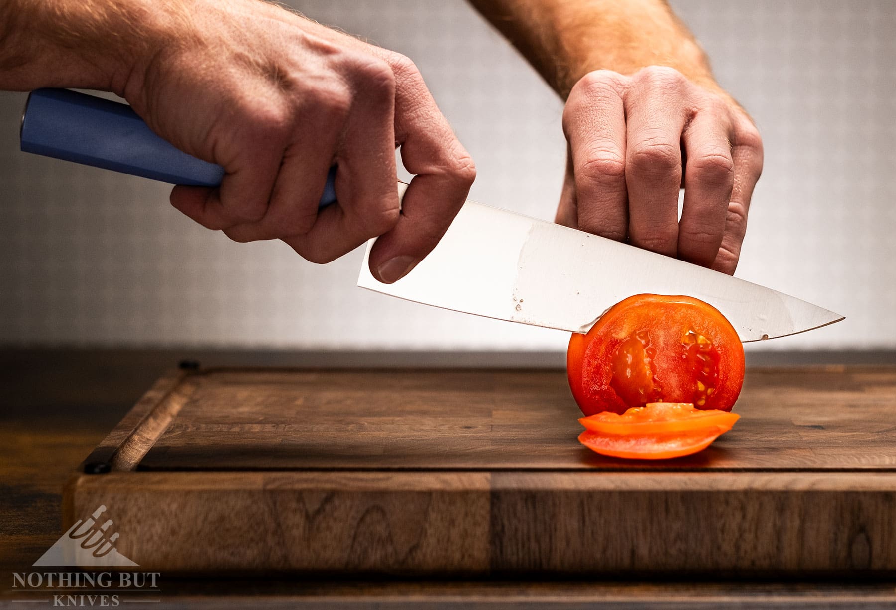 The Butterfork chef knife with a blue handle being used to slice a tomato.