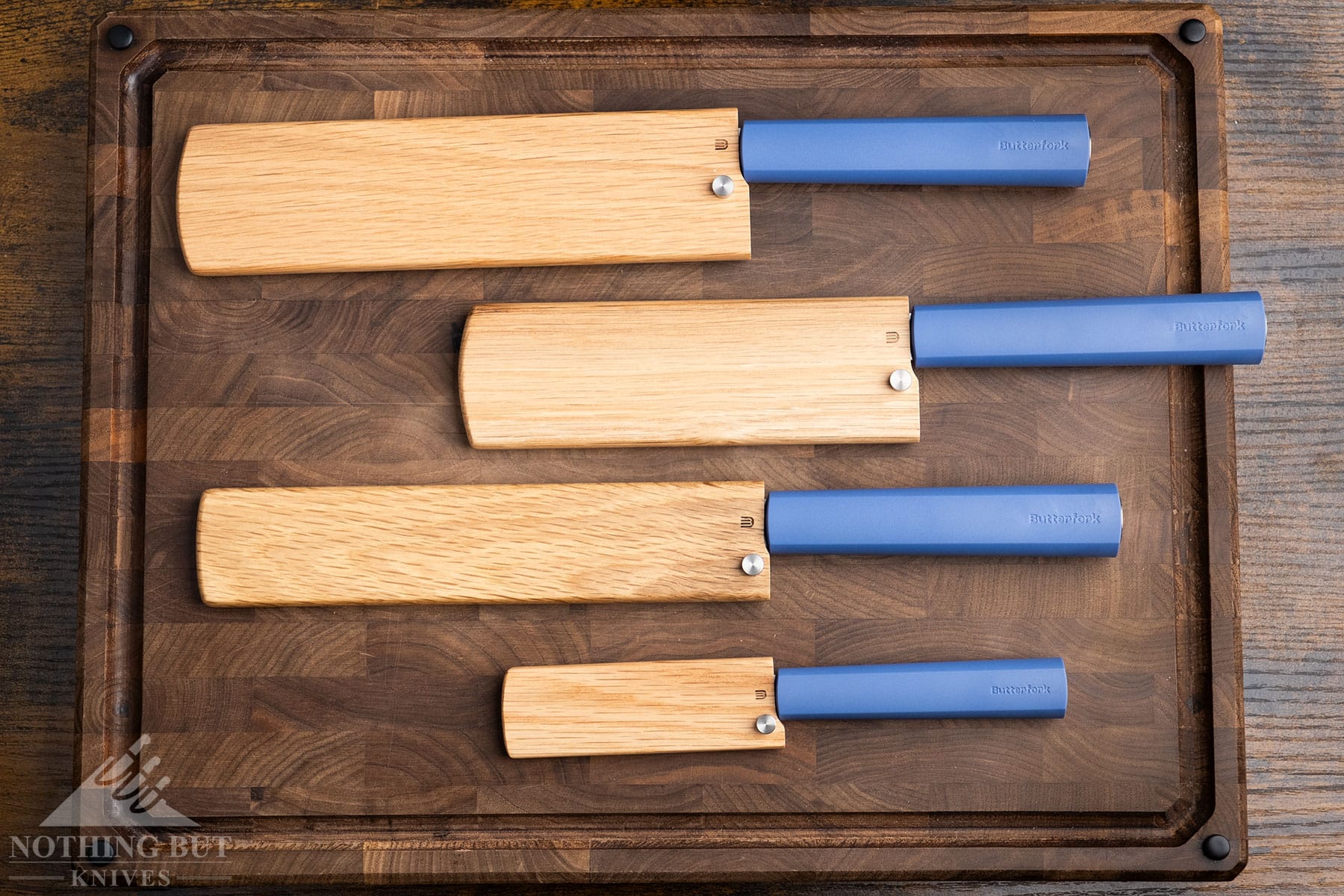 An overhead view of four Butterfork knives with their Oak covers on top on an end grain cutting board. 