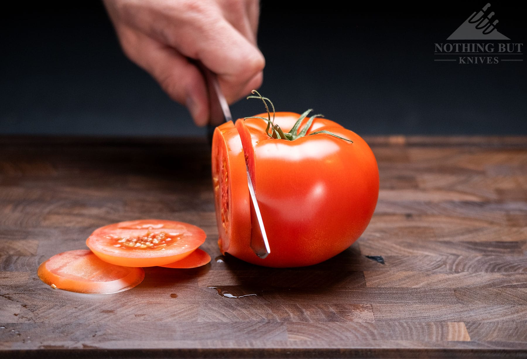 The Cangshan TC chef knife being used to slice a tomato with the point of the knife facing the camera.