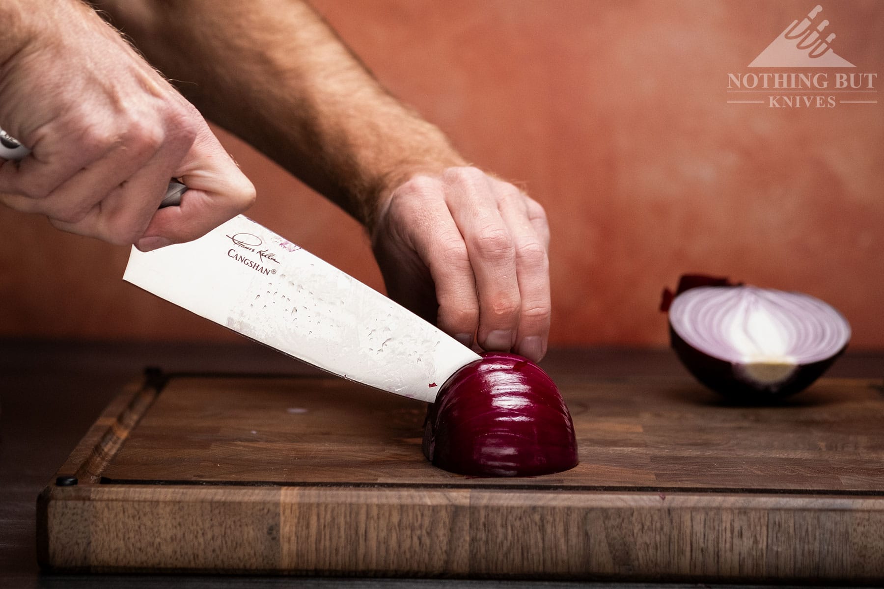The Cangshan Thomas Keller chef knife being used to make small slices in a red onion on a wood cutting board.