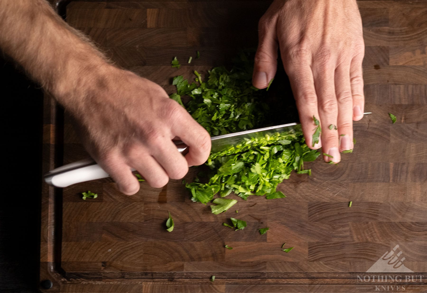 A top-down view of a professional Cangshan kitchen knife being used to rock chop green onions.