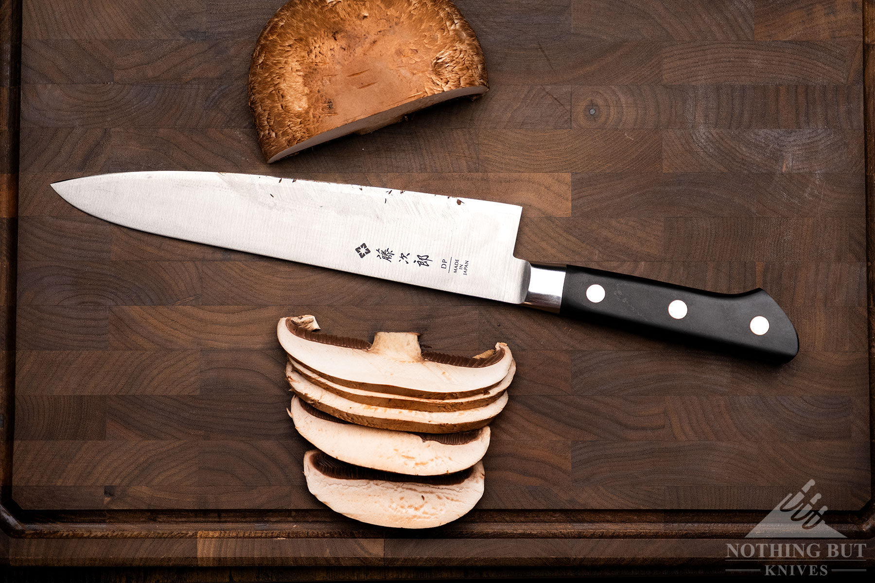 An Overhead view of a portobello mushroom that has been cut into slices by the Tojiro chef knife which is sitting between the two parts of the mushroom. 