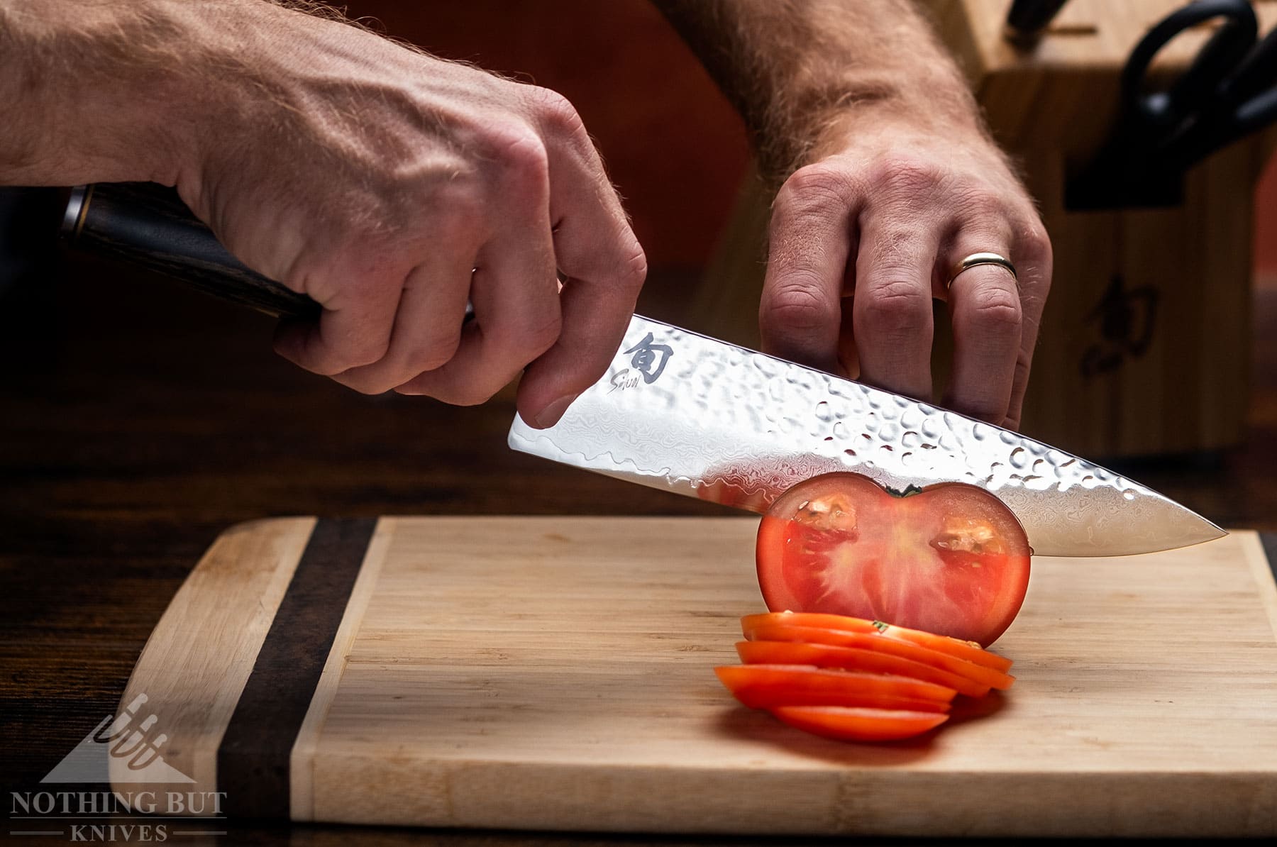 The Shun Premier chef knife being used to slice a tomato on a wood cutting board in front of the rest of knife set.