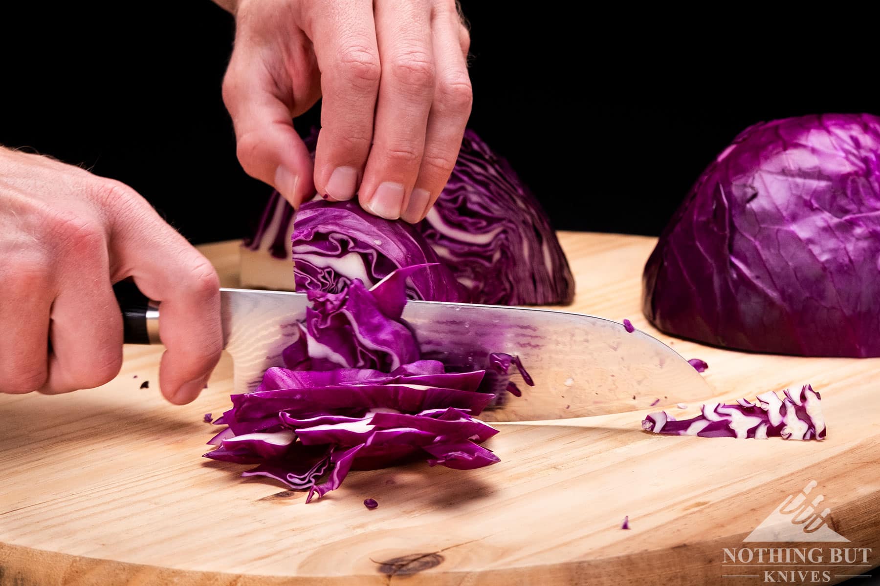 The Shun Classic chef knife slicing red cabbage on a wood cutting board.