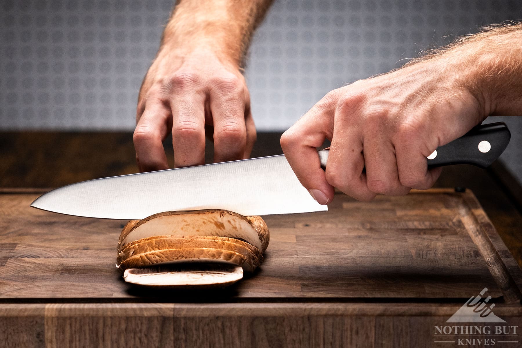 A close-up of the Tojiro DP chef knife being used to slice a portobello mushcroom on a wood cutting board in front of a white background. 