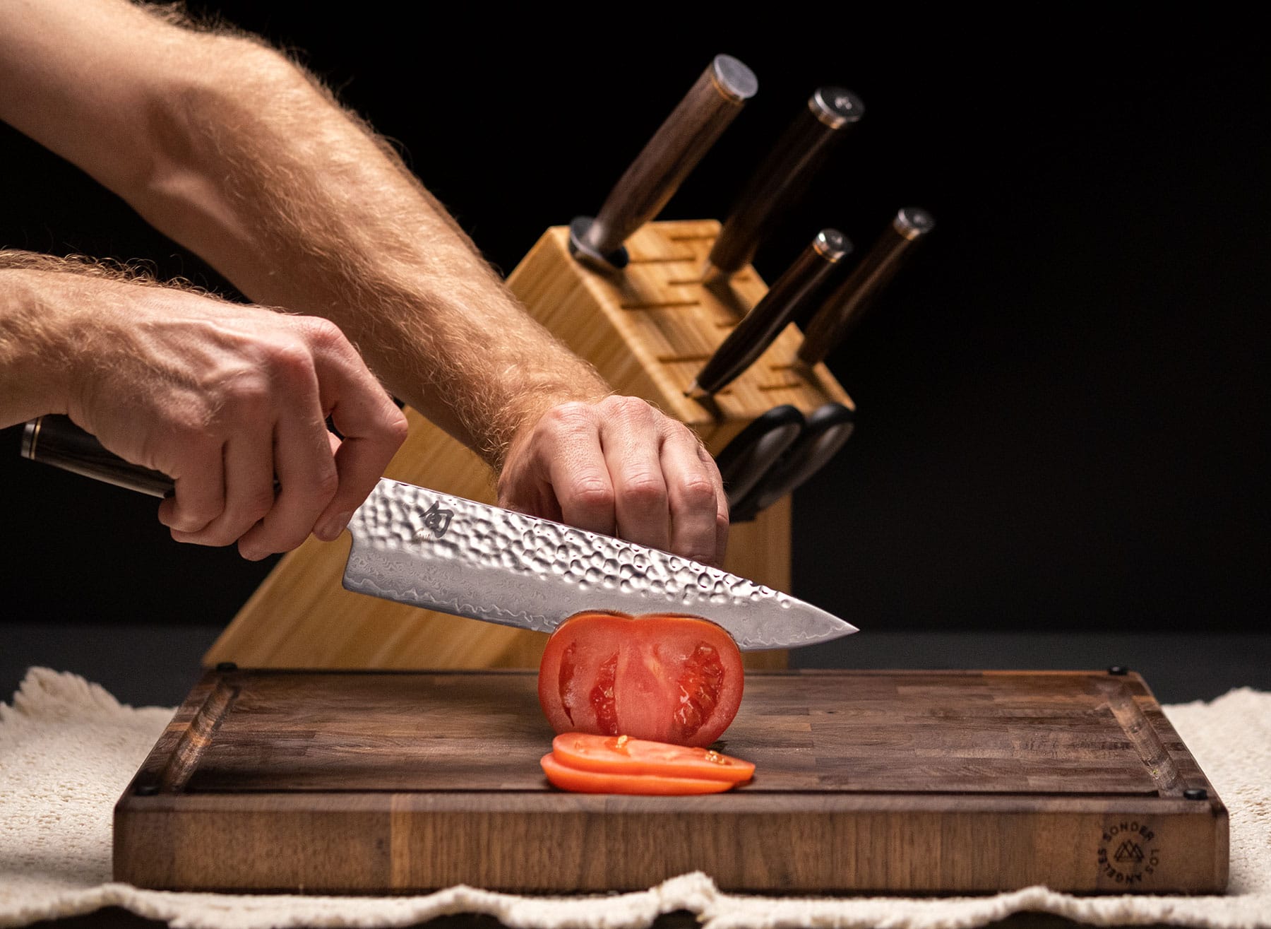 Slicing a tomato with the Miyabi Mizu chef knife in front of the set and storage block.