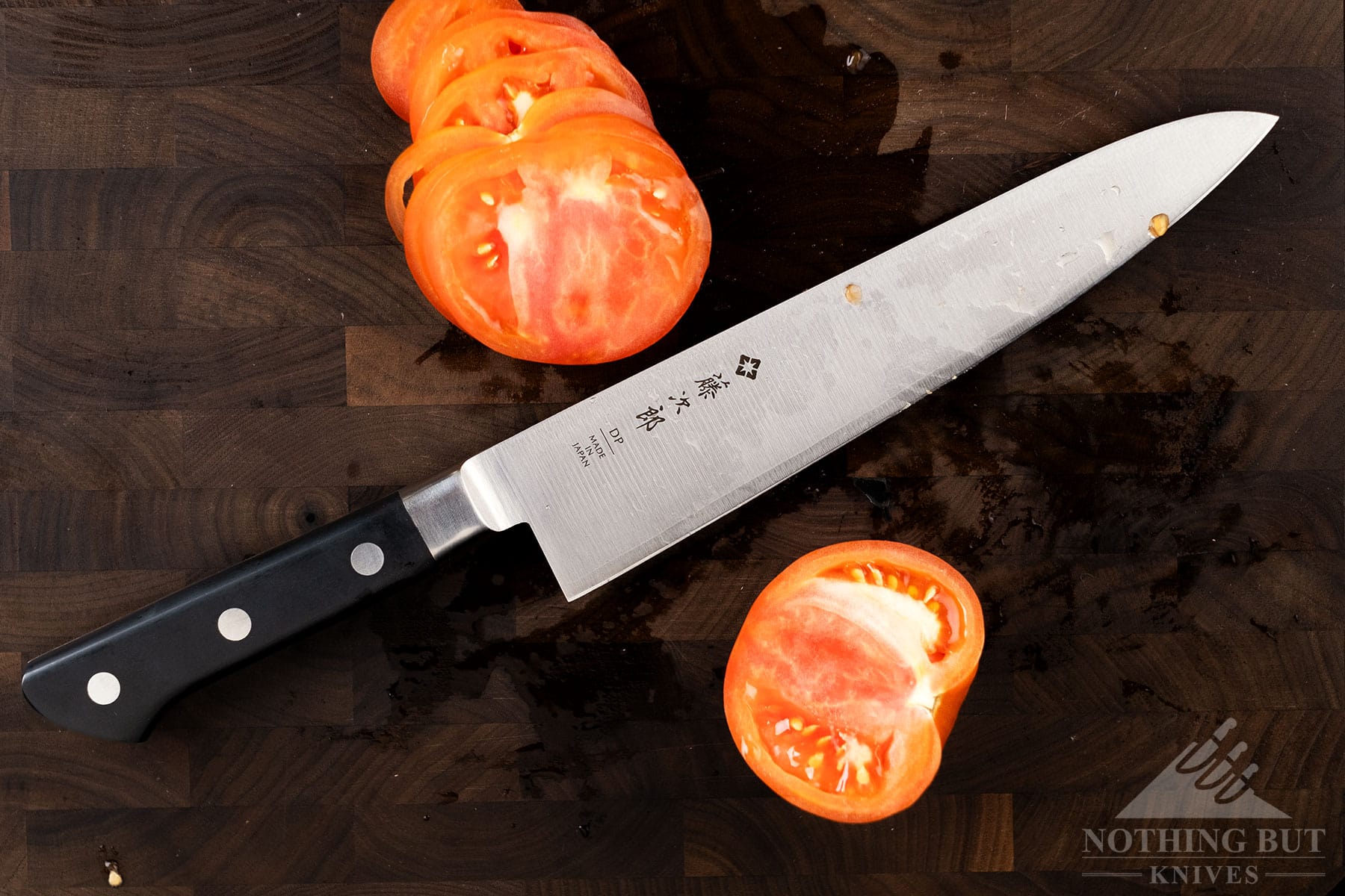 The Tojiro DP F808 8-inch chef knife on a cutting board between two sections of a tomato it was used to slice.