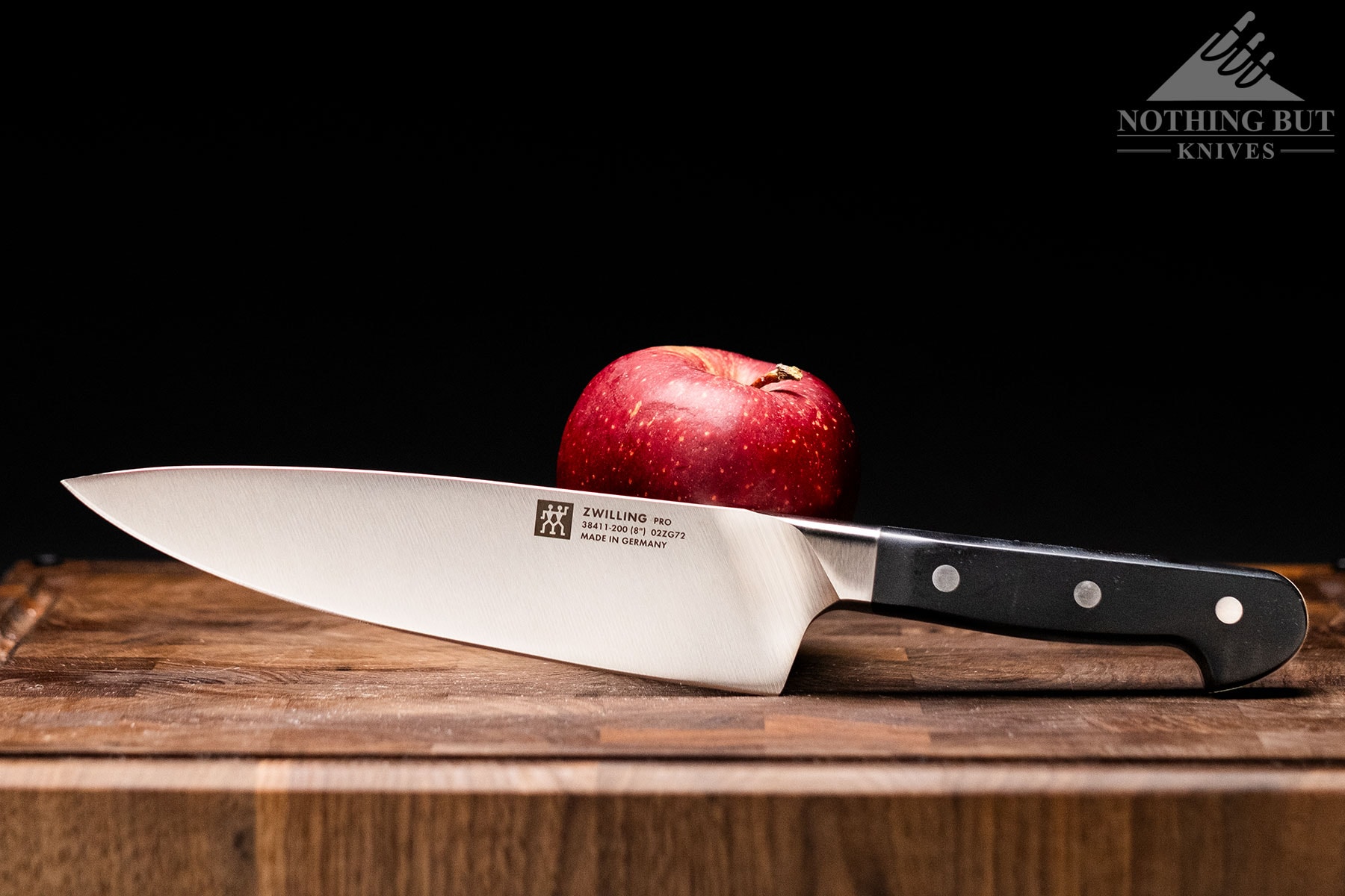 The Zwilling Pro 8-inch chef knife with a red apple on a wood cutting board in front of a dark background.