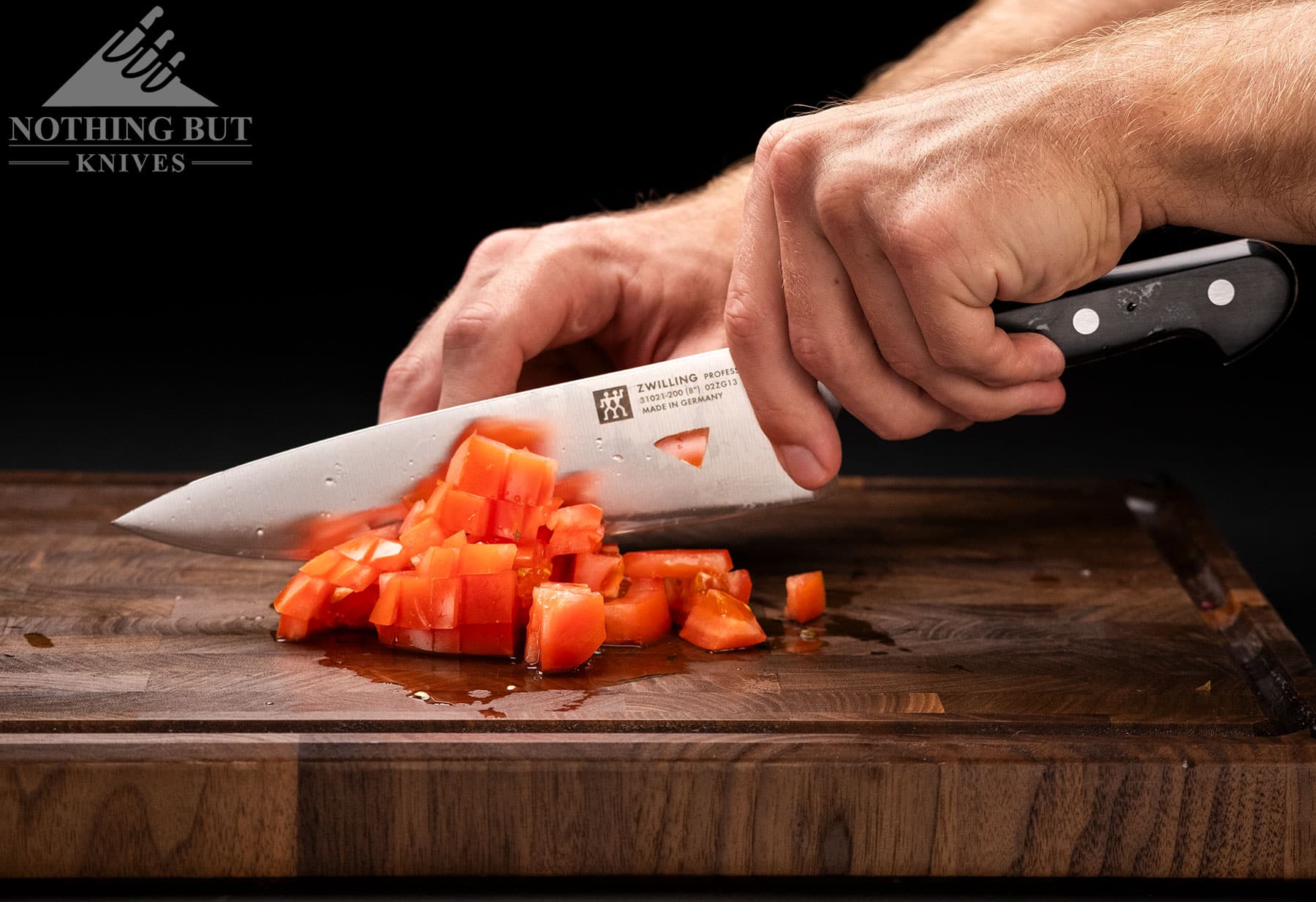A close-up of the Zwilling Professional S chef knife dicing a heirloom tomato. 