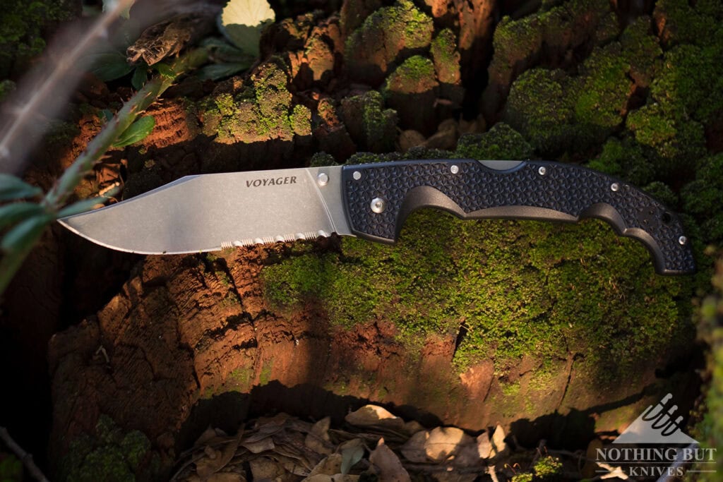 A large pocket knife with the blade open on a moss-covered rock.