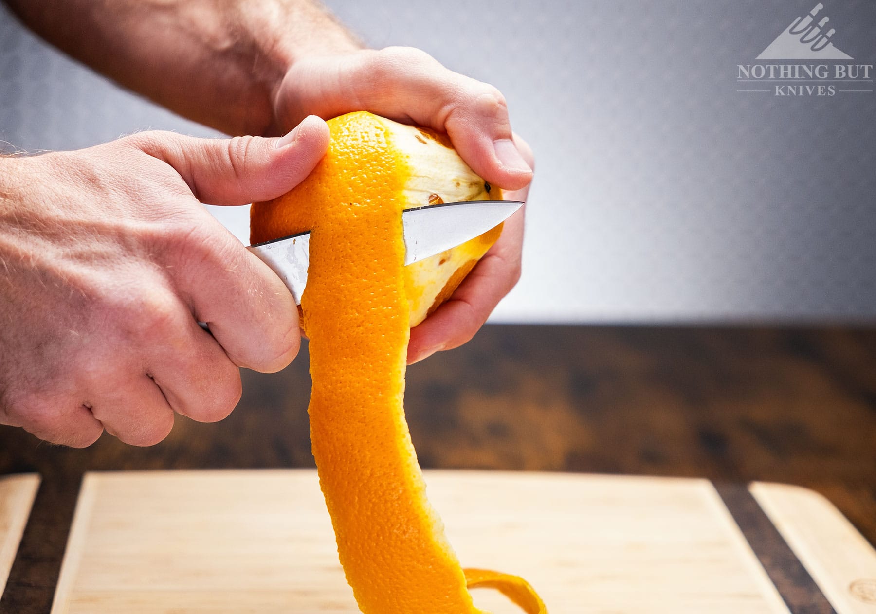 A close-up of the Tojiro DP Damascus steel chef knife peeling an orange above a bamboo cutting board. 