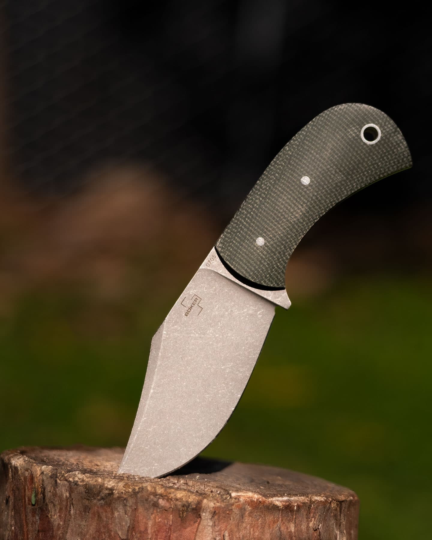 The Boker Plus Madman with green Micarta handle scales sticking out of a tree stump.
