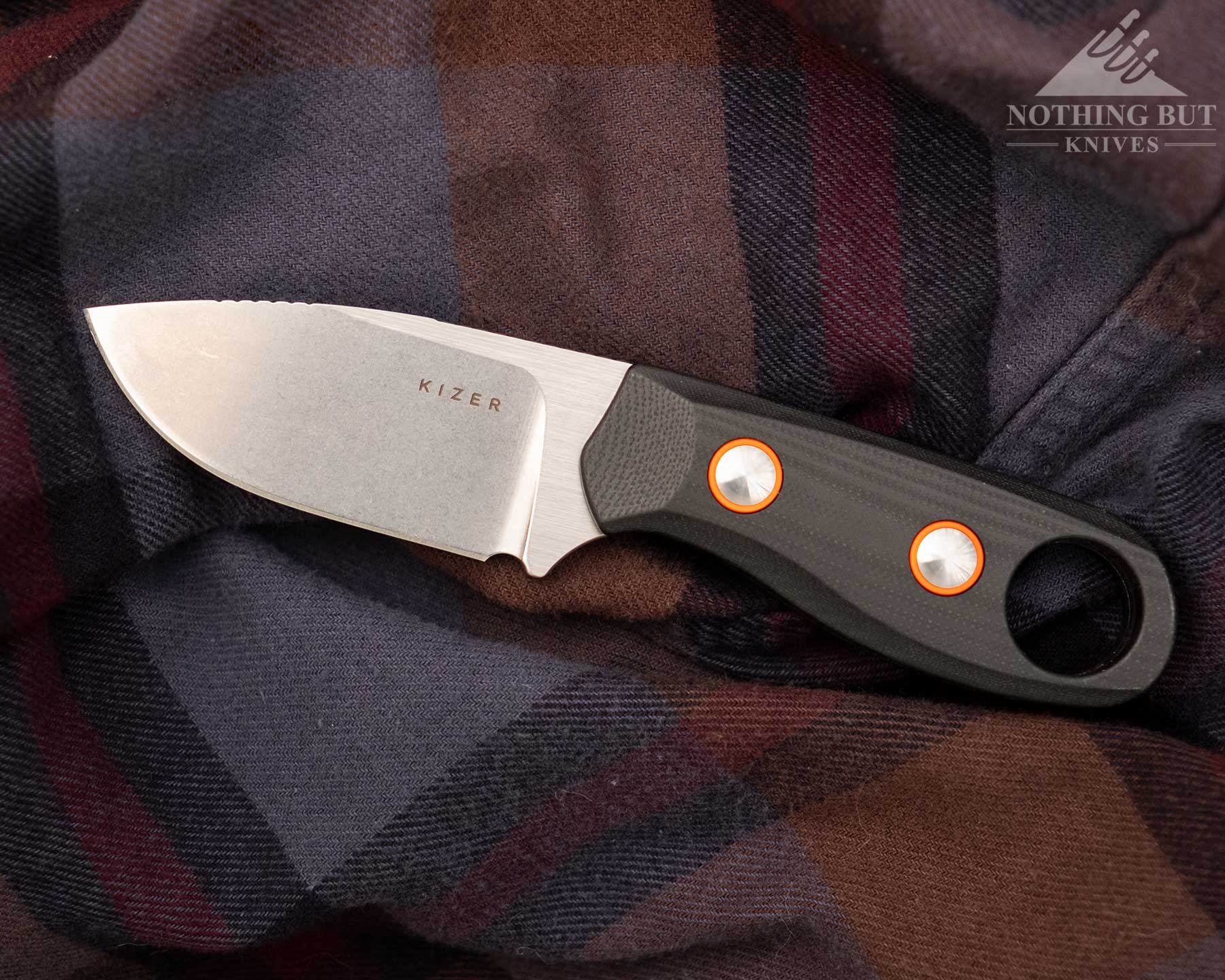 An overhead view of the Kizer Beaver fixed blade EDC knife on a blue and red flannel shirt. 