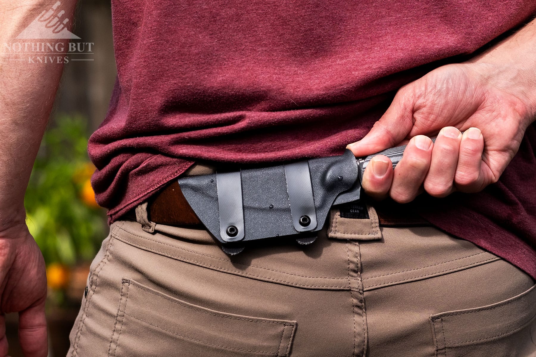 The Kizer Harpoon fixed blade knife being deployed from its sheath in the small of a person's back. 