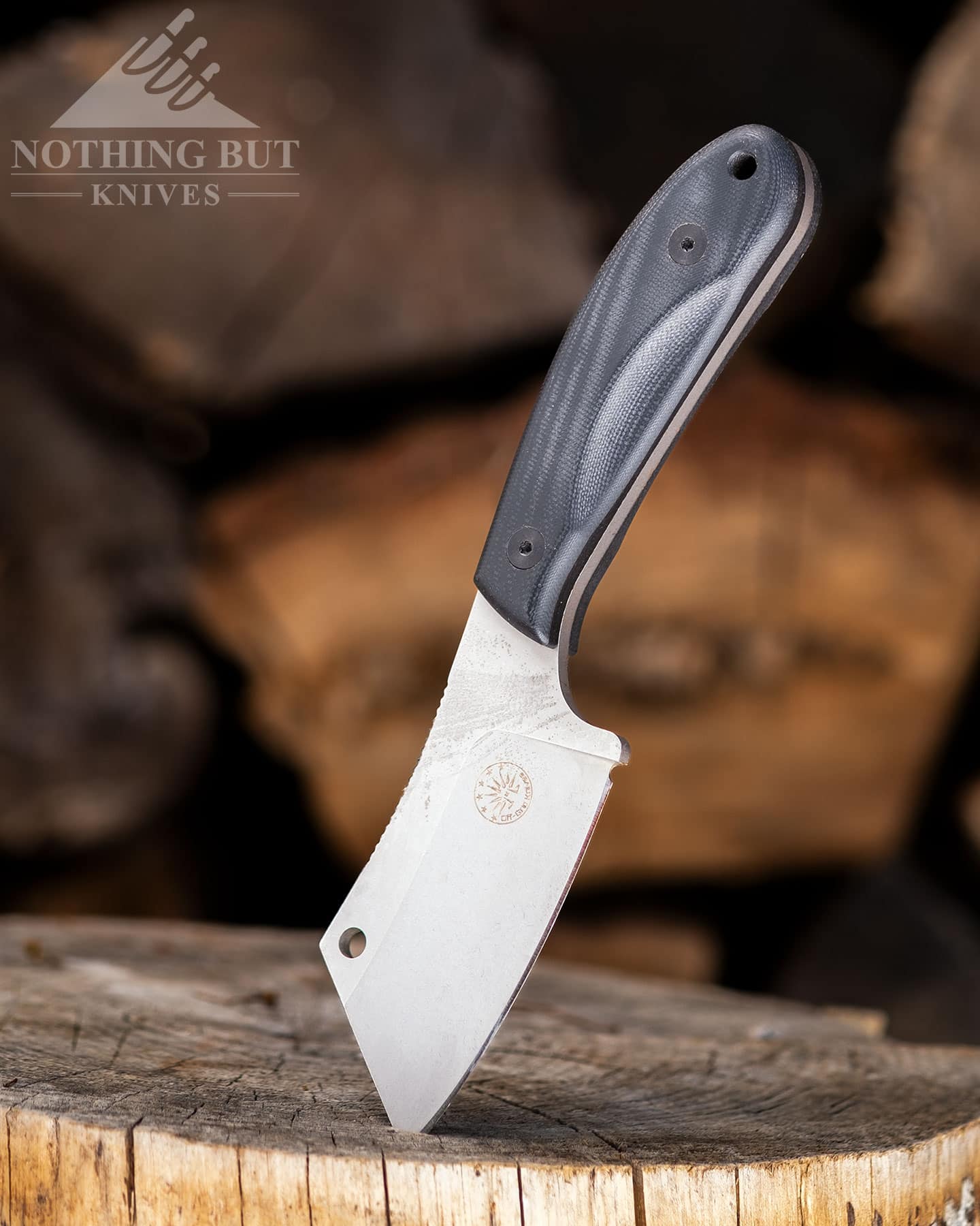 The Off-Grid Hoglet cleaver style fixed blade knife with its blade stuck in a tree stump in front of a firewood pile.
