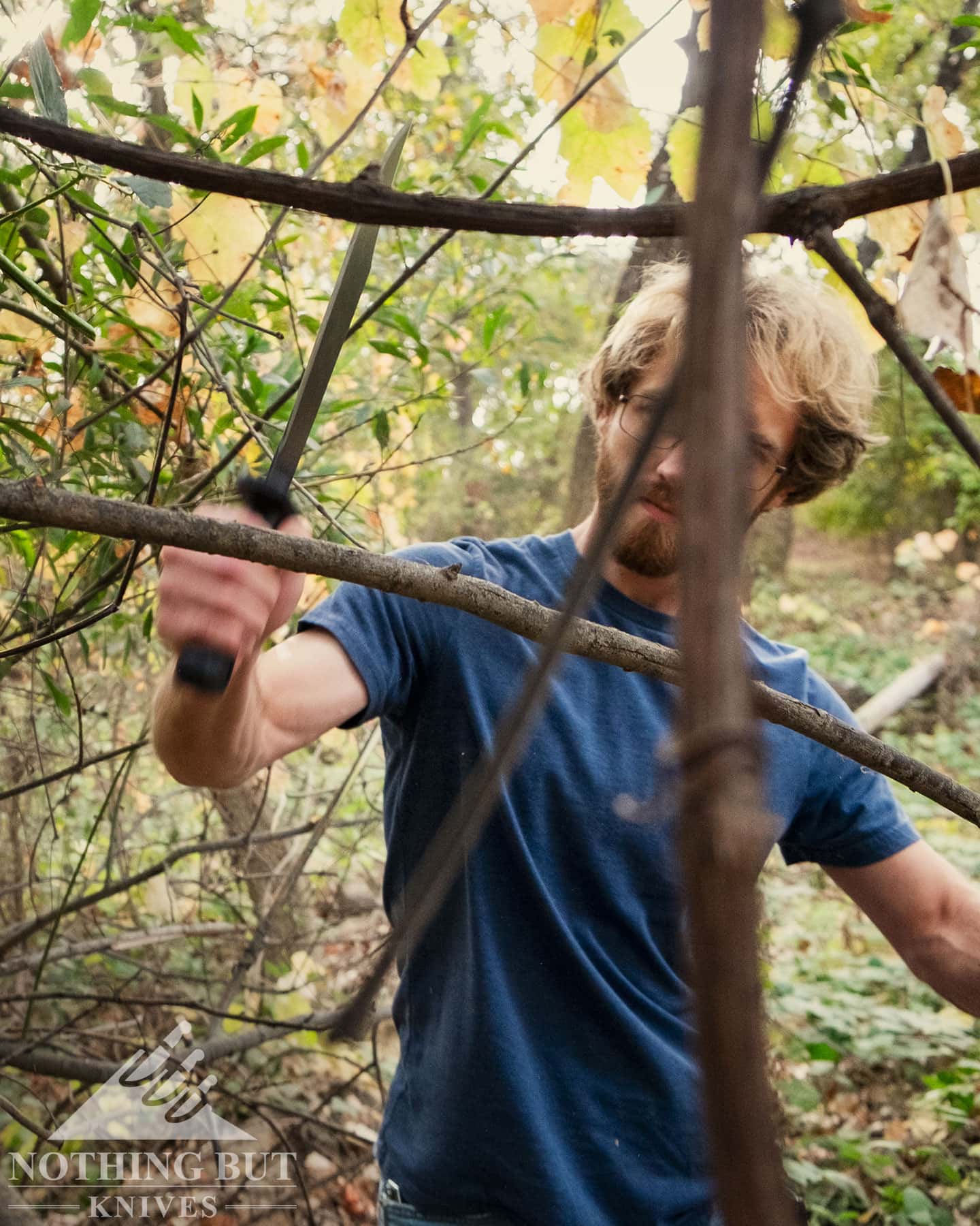 A person using the Cold Steel Black Bear Bowie to clear vines in a forest.