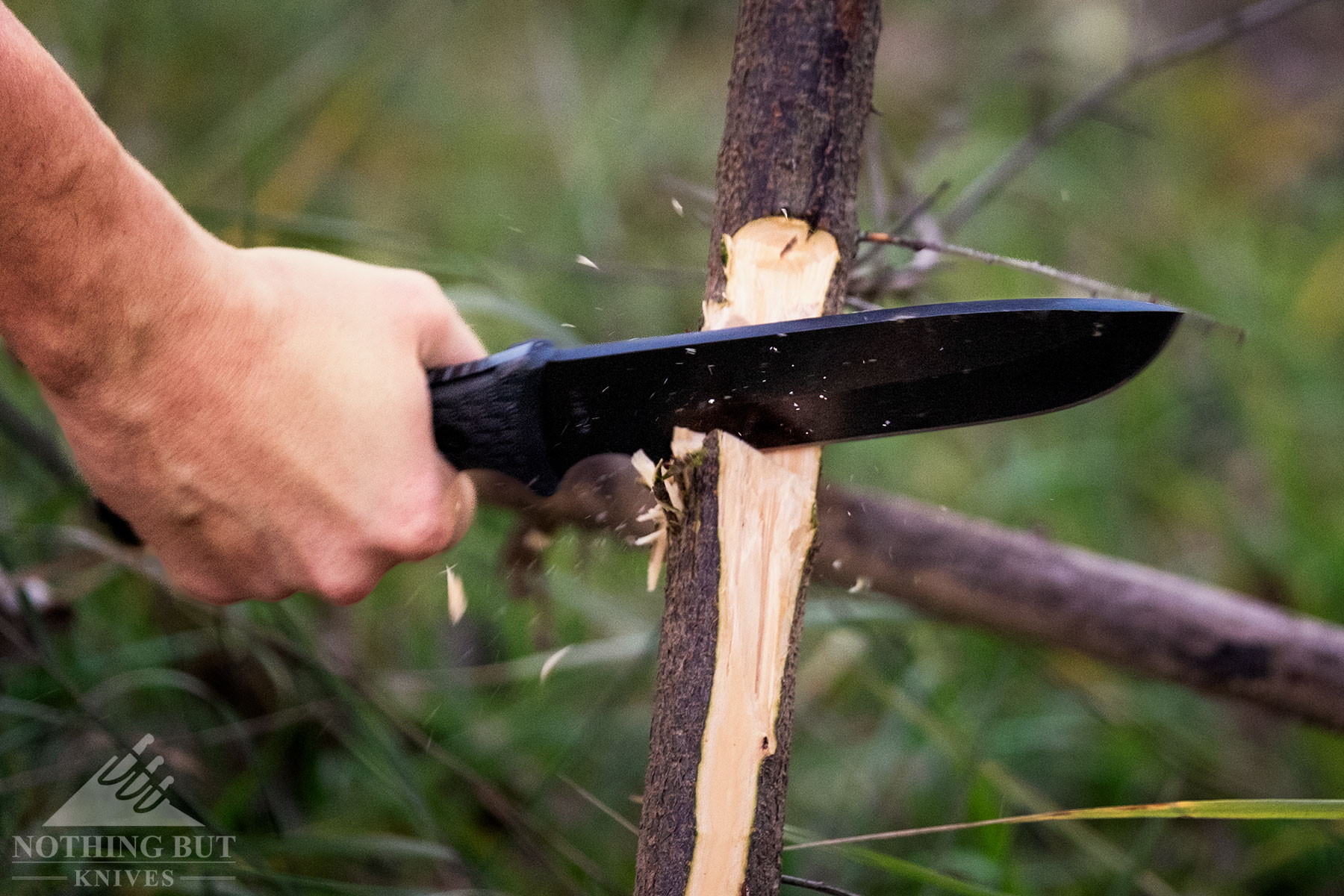 The Schrade SCHF 52 chopping through a vine with a blurred green field in the background.