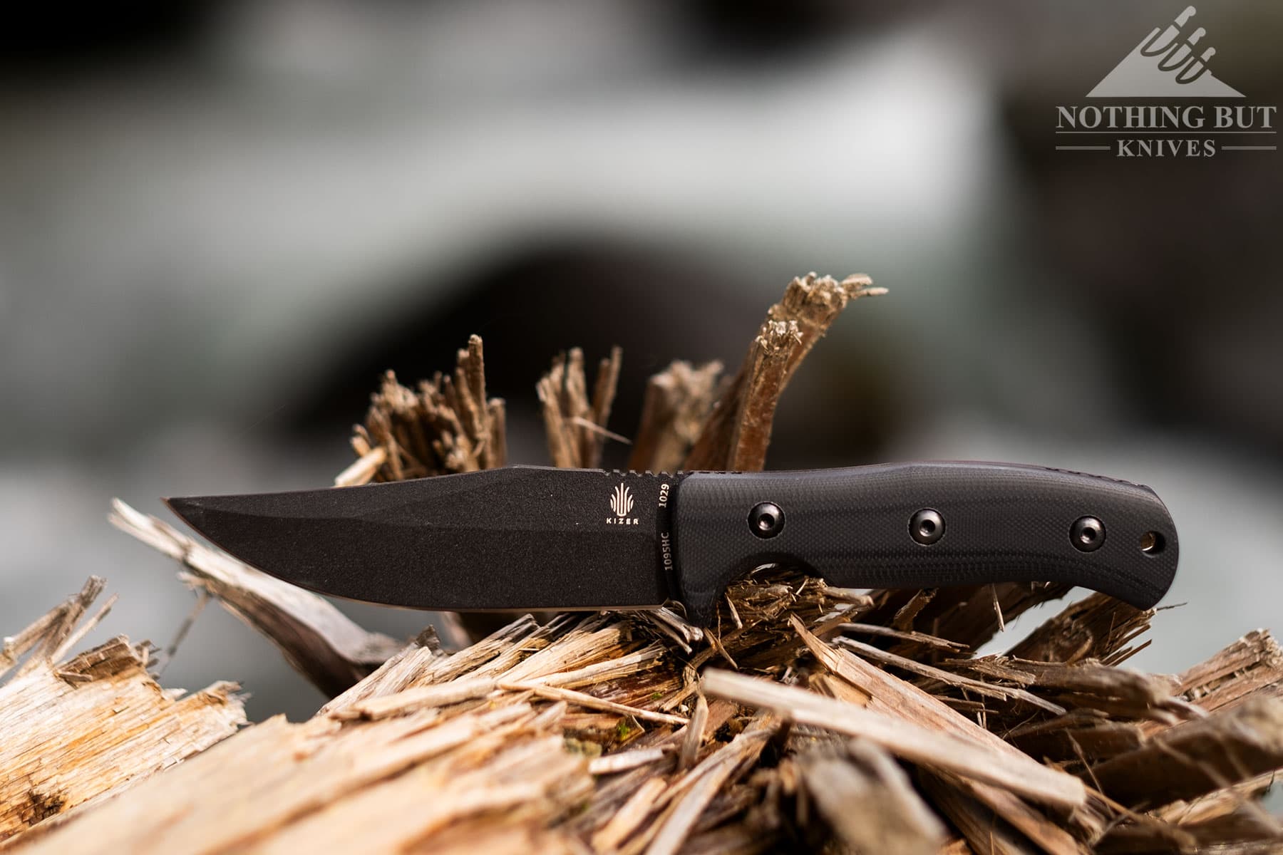 The Kizer Little River Bowie compact knife sitting on a splintered log with its blade tip pointing to the left. 