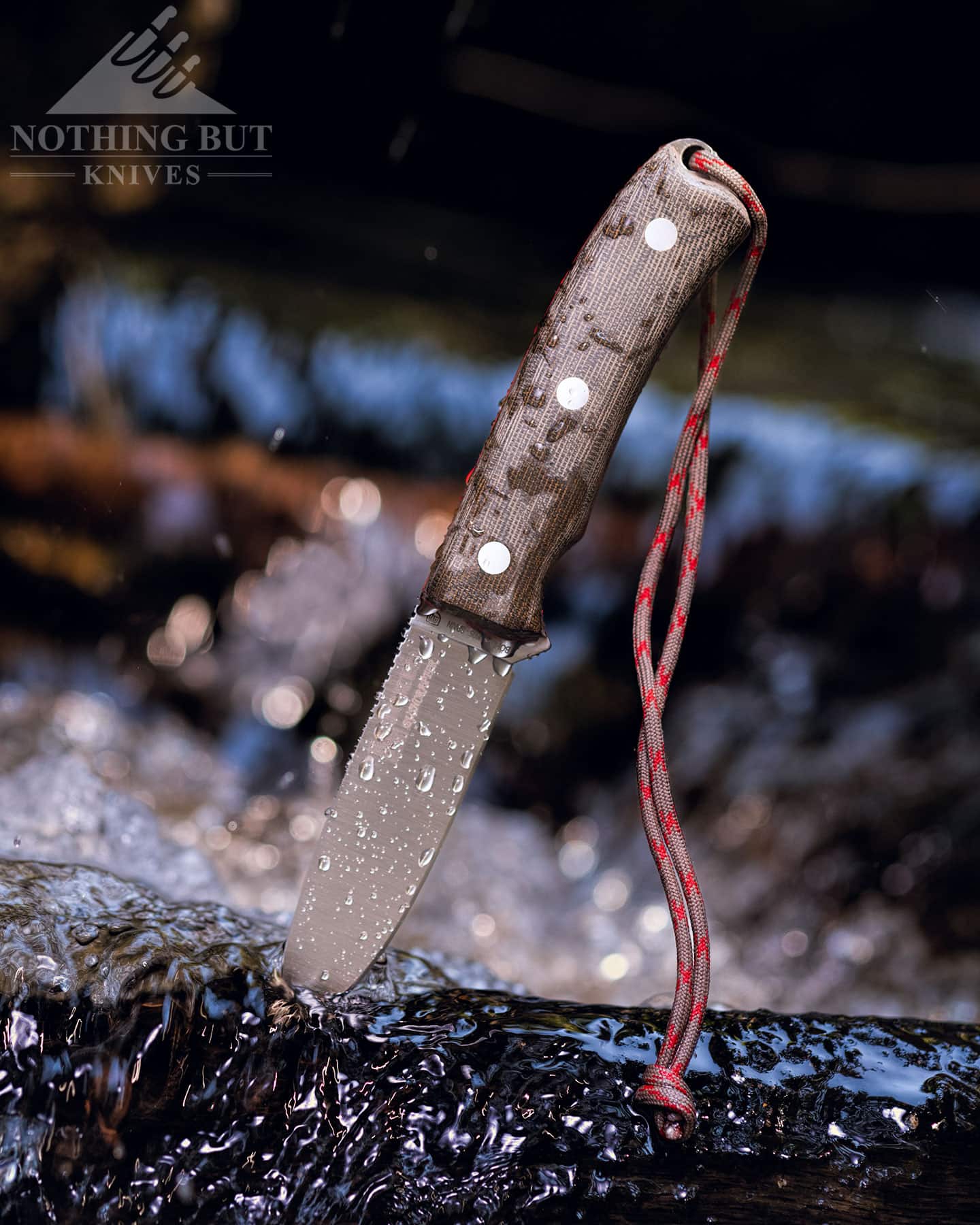 The Joker Bushcrafter knife with its blade stuck in a piece of wood in a mountain creek causing its Micarta handle scales to get wet. 