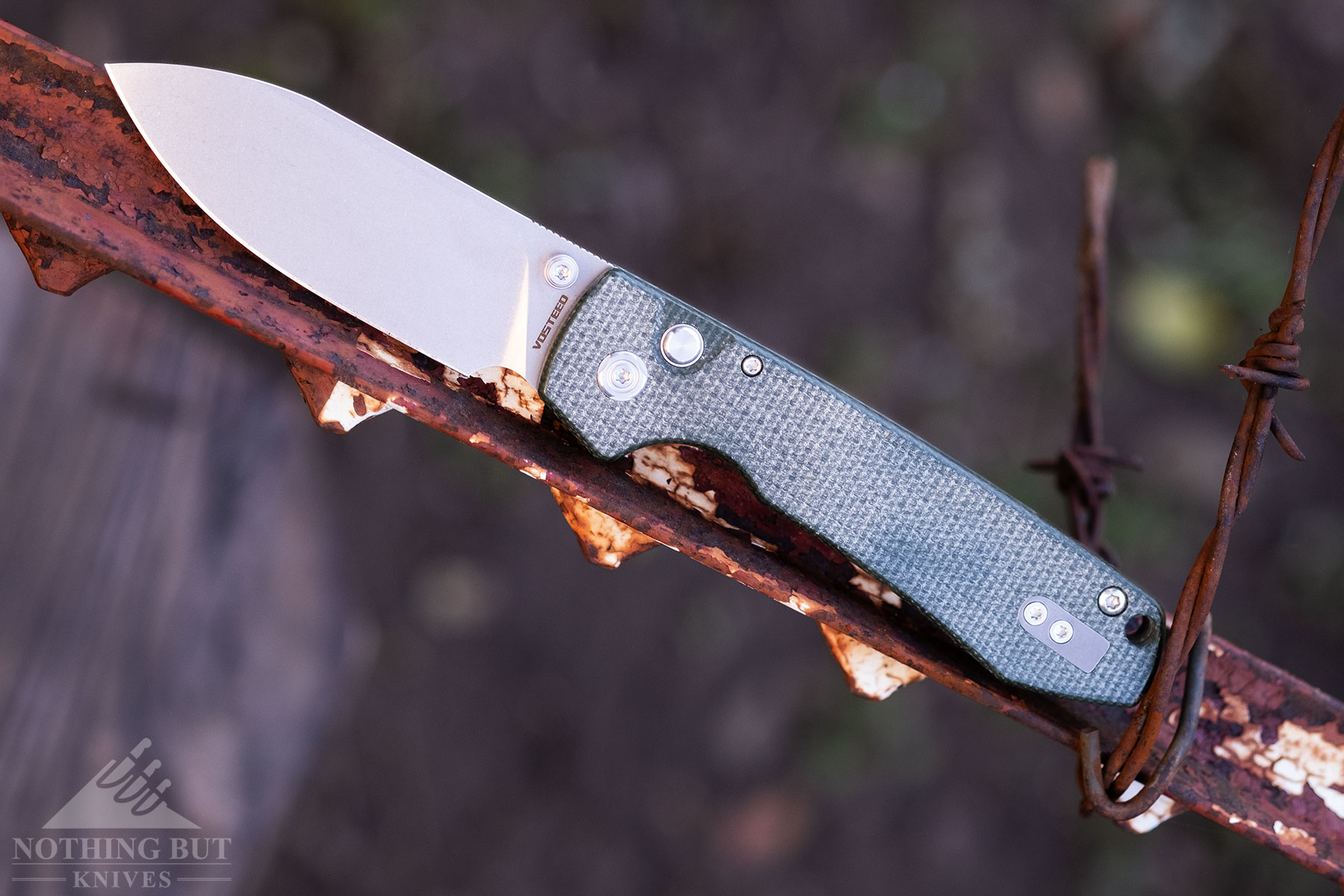 The Vosteed Racoon with green Micarta handle scales shown here with the blade in the open position balanced on a rusty fence post.