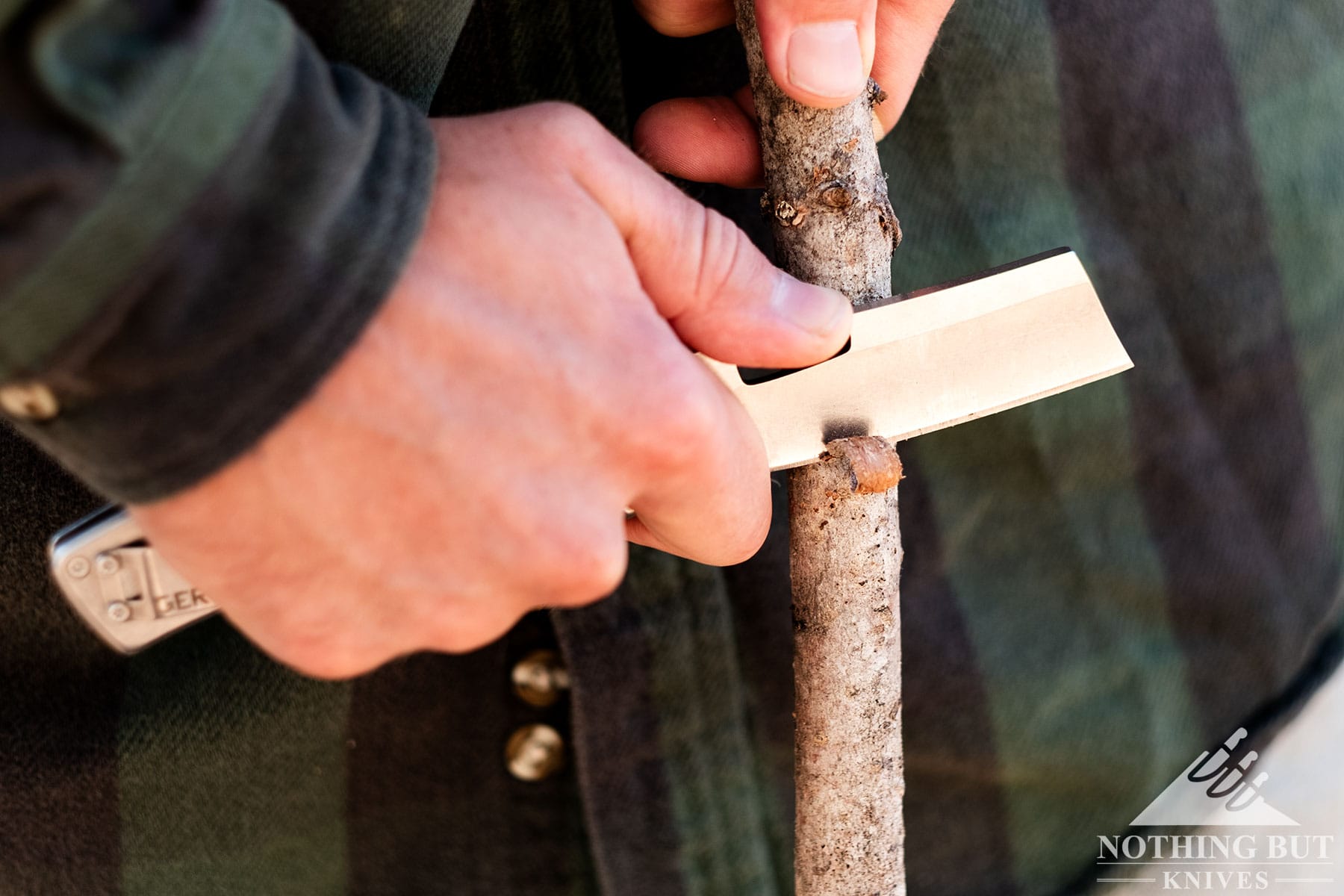 A close-up of the Gerber Flatiron pocket cleaver in a person's hand being used to carve a stick. 