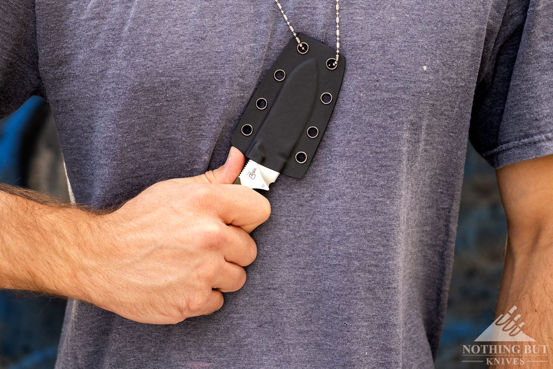 A close-up of the QSP Neckmuck being removed from its sheath hanging from a lanyard around a person's neck. 