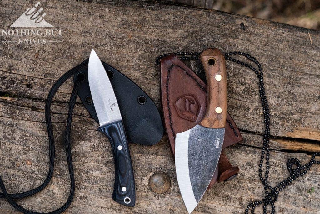 Two of our favorite neck knives with their sheaths on a wood table outdoors.
