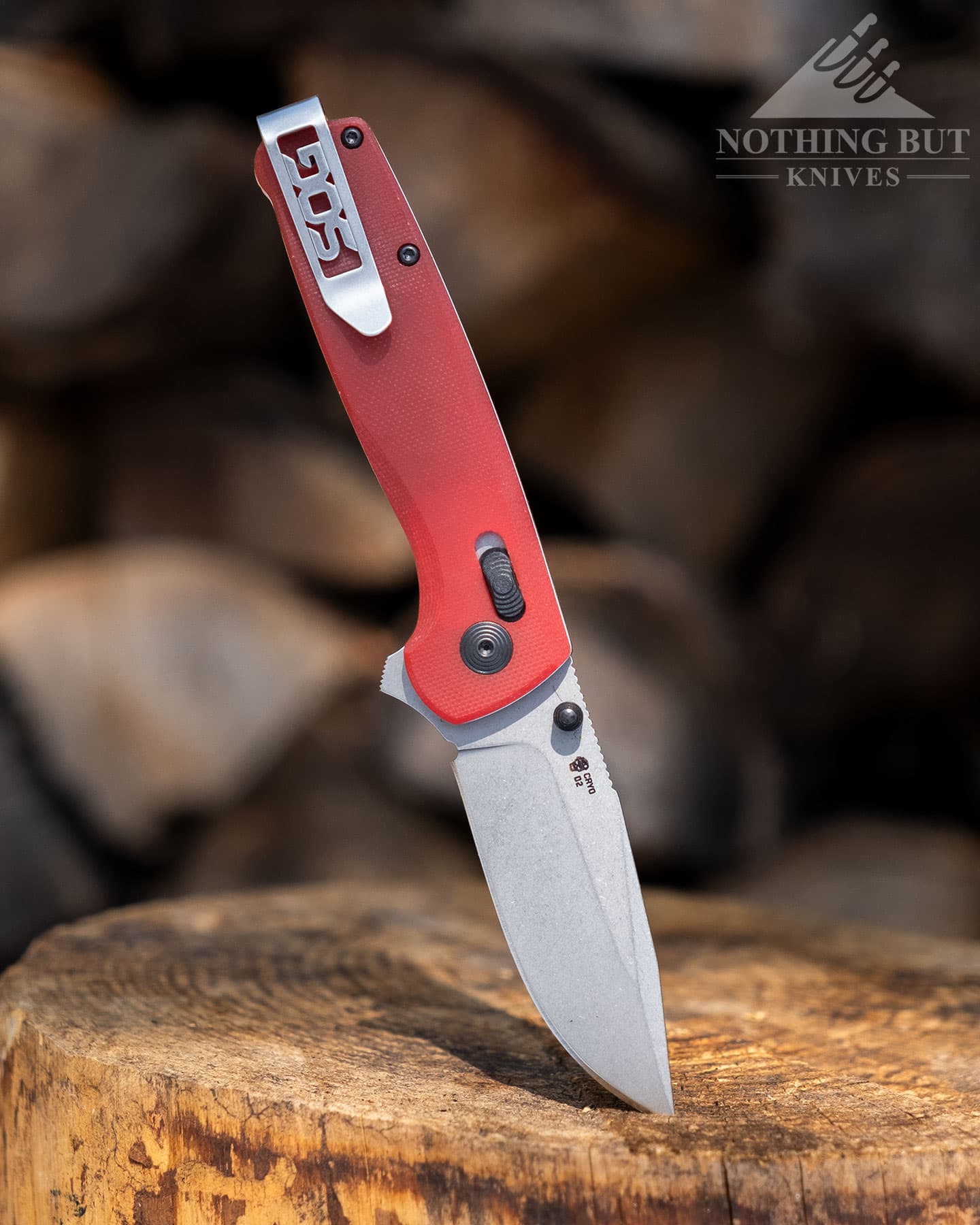 The SOF Terminus XR with red handle scales shown here with the tip of the blade sticking out of the top of a tree stump in front of a firewood pile. 