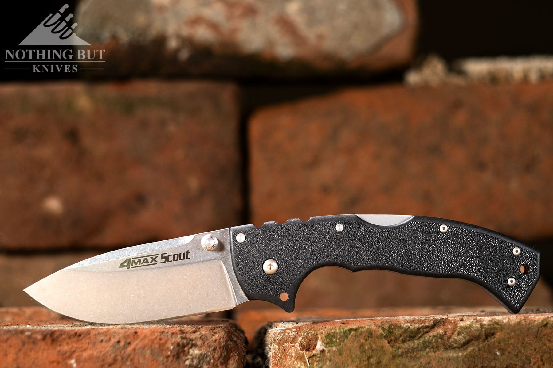 A big folding knife in the open position on a brick in front of a brick background.