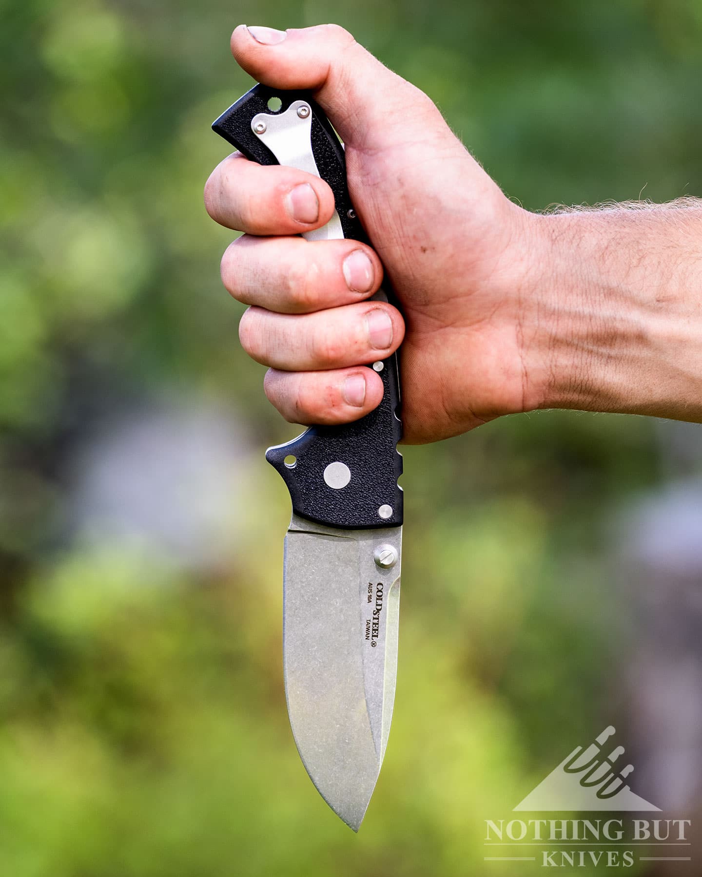 The Cold Steel 4-MAX Scout being held in a reverse grip in a person's right hand.