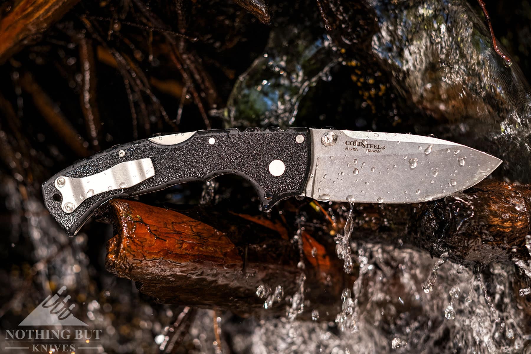 The Cold Steel 4-Max Scout pocket knife in the open position on a branch in a mountain creek.