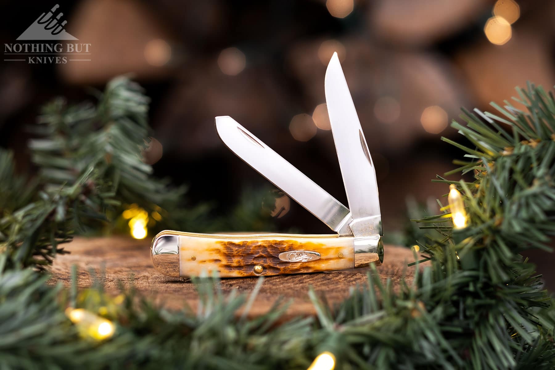 The Case Ampber Bone Trapper slip joint knife shown here with both blades in the half open position on a tree stump with Christmas lights. 