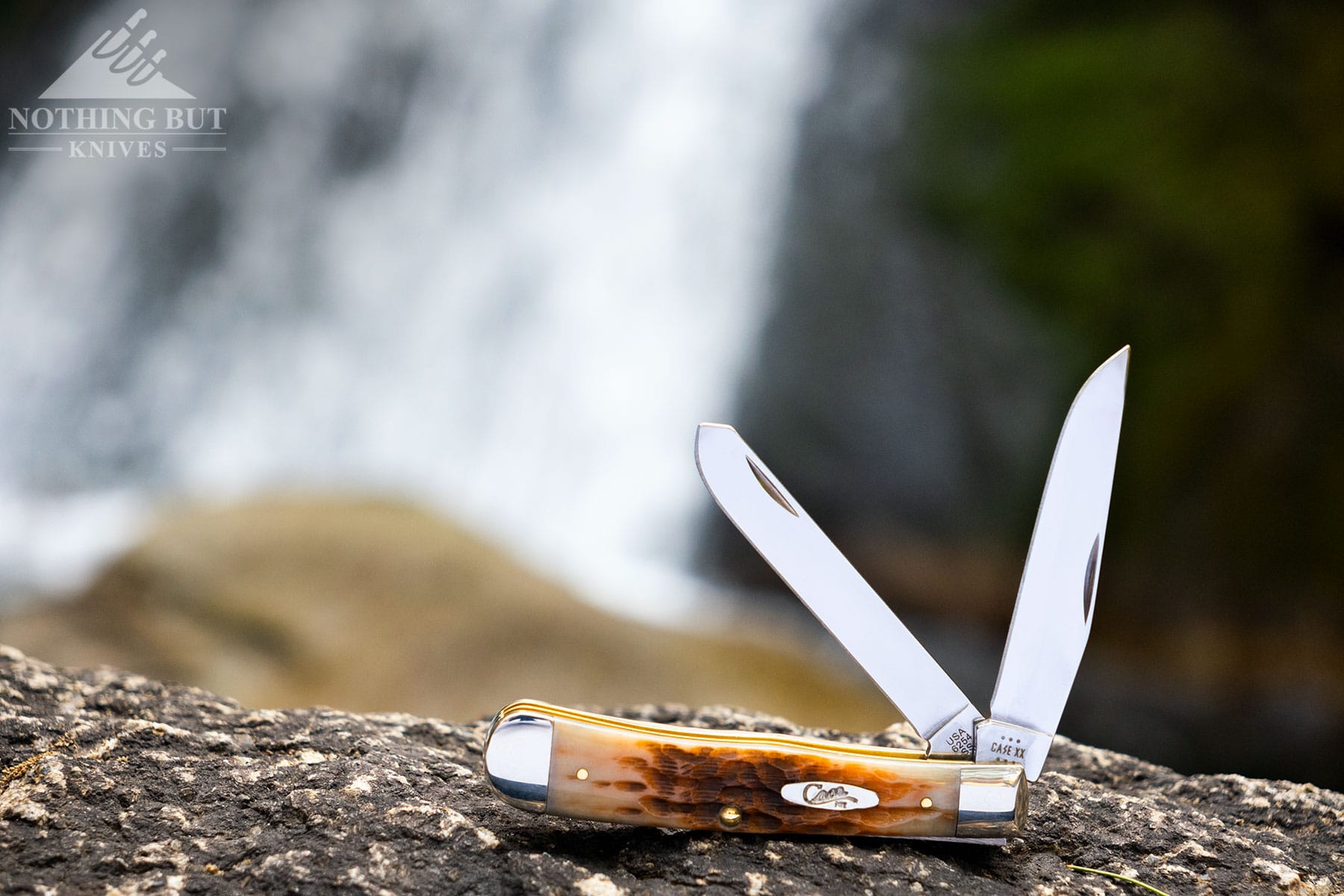 The Case Trapper slip joint knife with both blades half open sitting in front of a waterfall. 