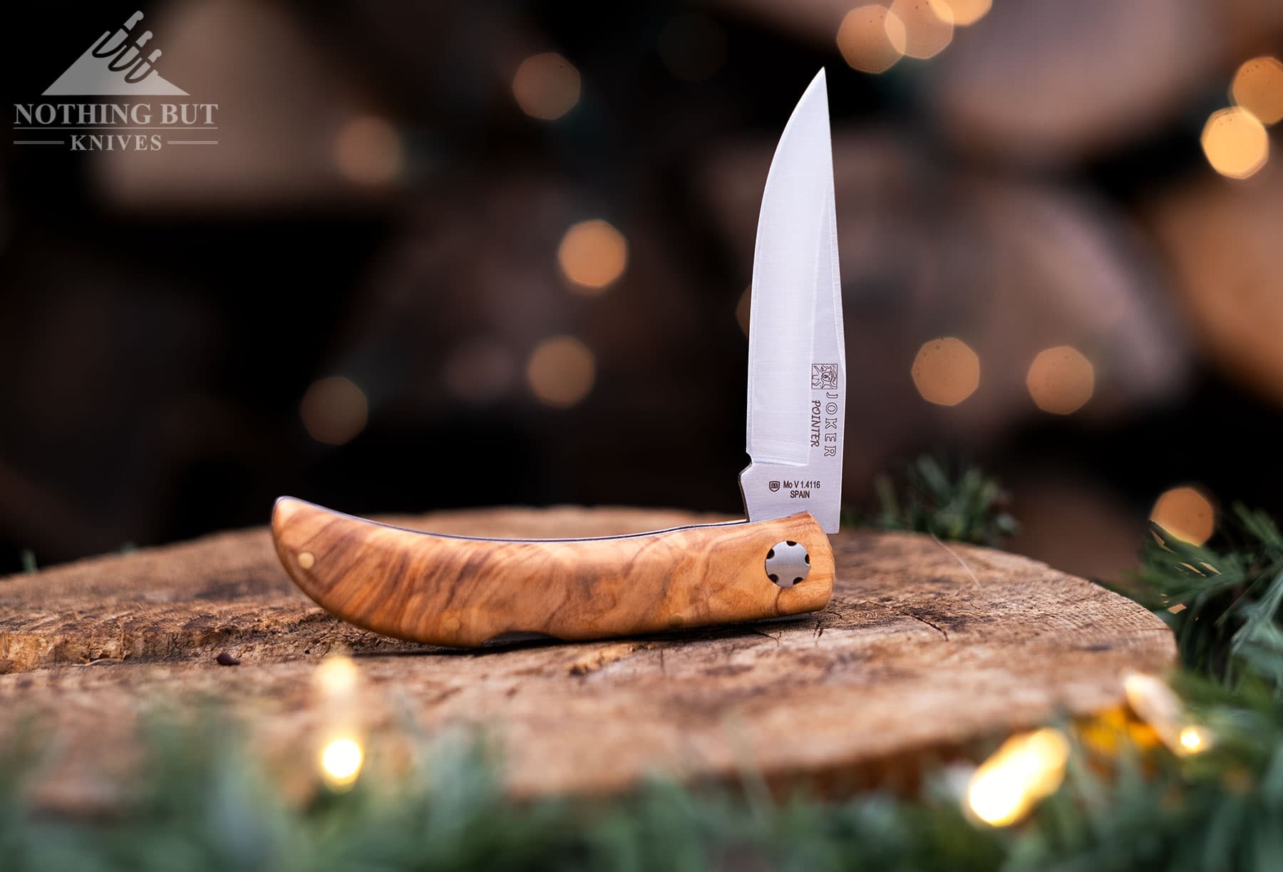 The Joker Pointer backlock EDC knife with the blade in the half open position on top of a holiday decorated tree stump. 