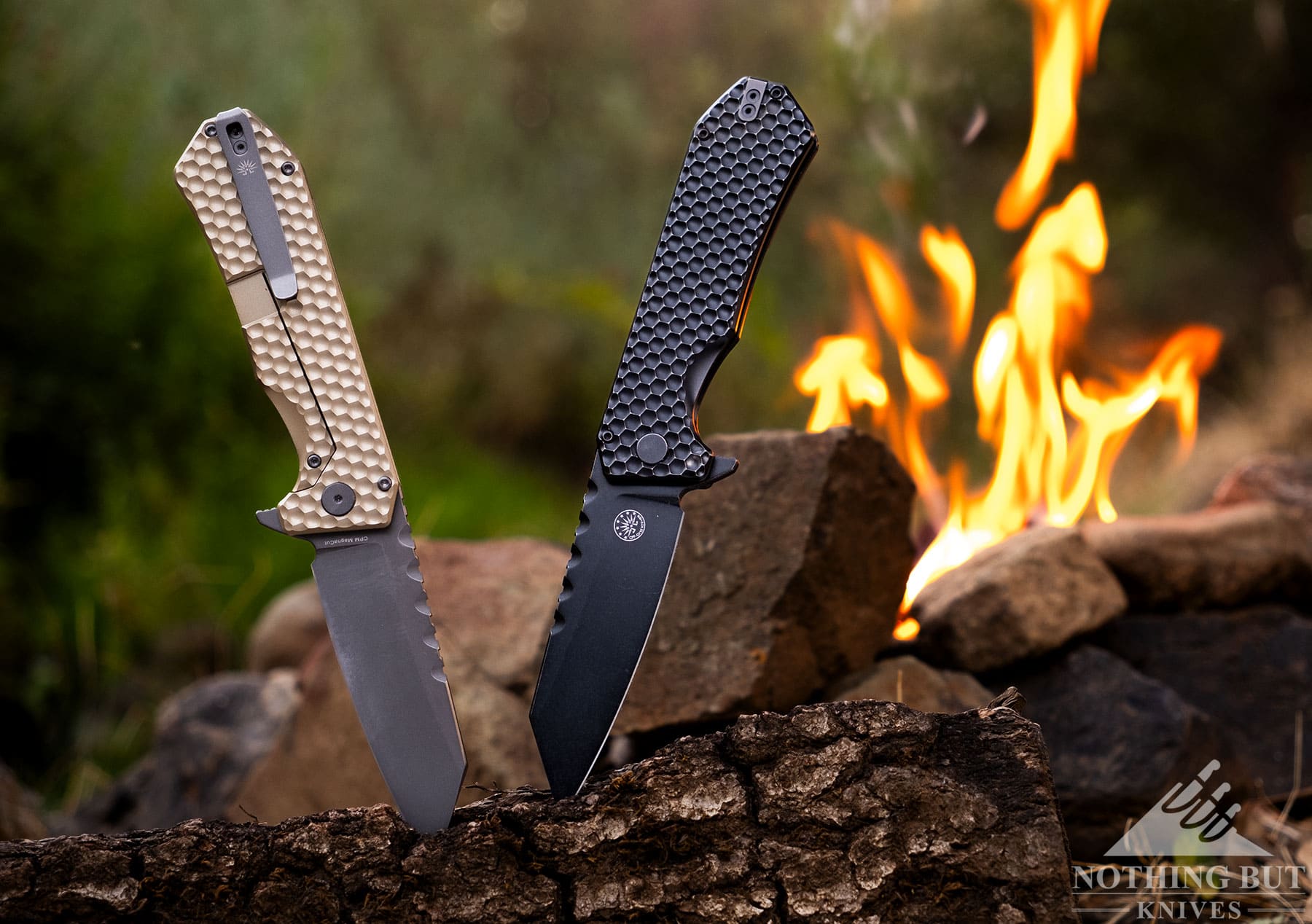 The two version of the Off-Grid Black Mamba V3 sticking out of a piece of firewood in front of a campfire. 