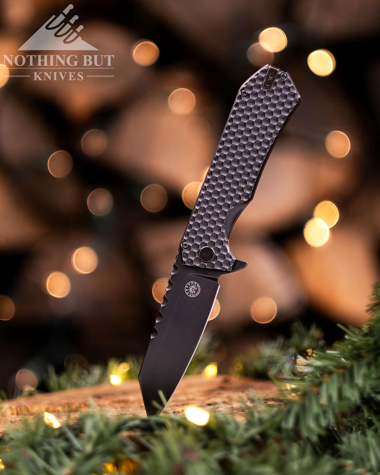 The Off-Grid Black Mamba V3 tactical knife sticking out of a tree stump decorated with garland in front of blurry holiday lights. 