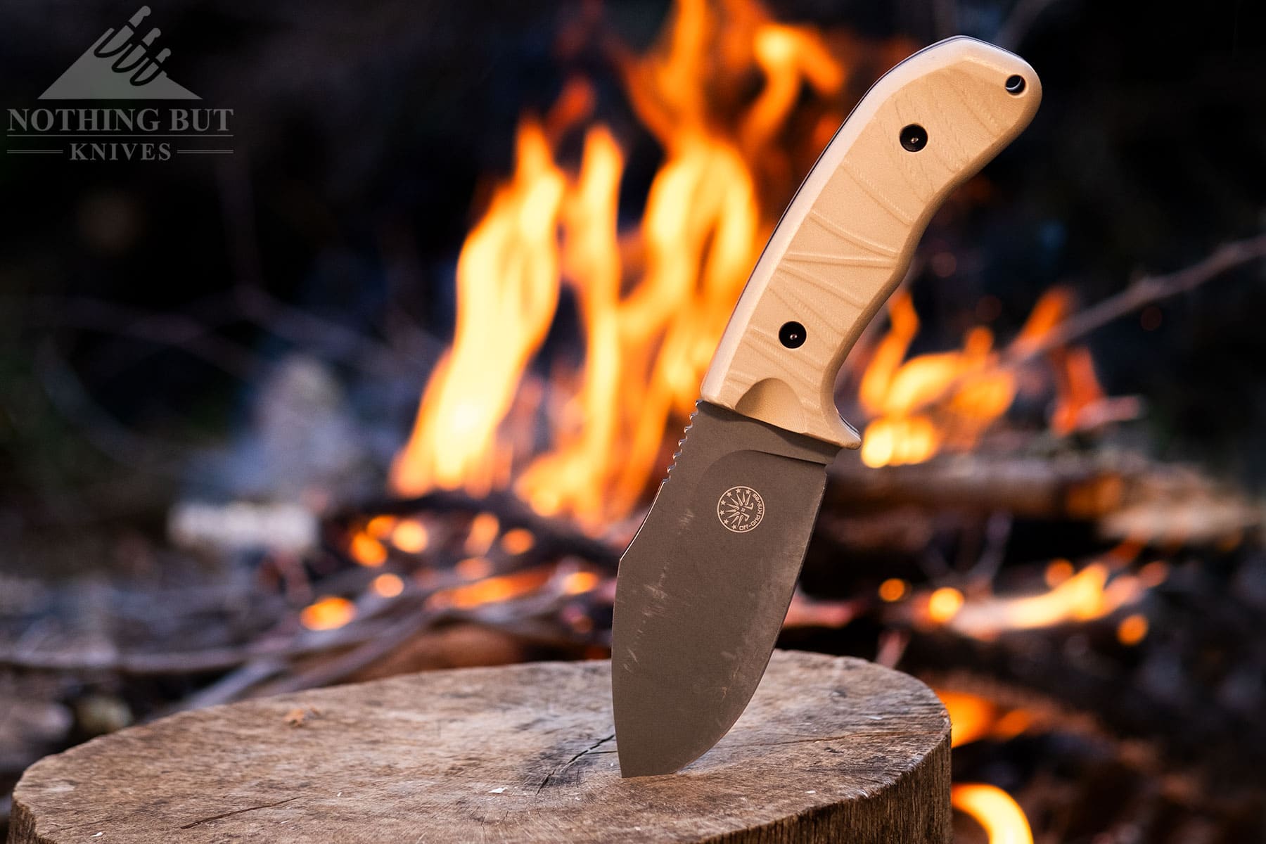 The Off-Grid Alpha-Dog fixed blade knife shown blade down on a tree stump in front of a campfire.