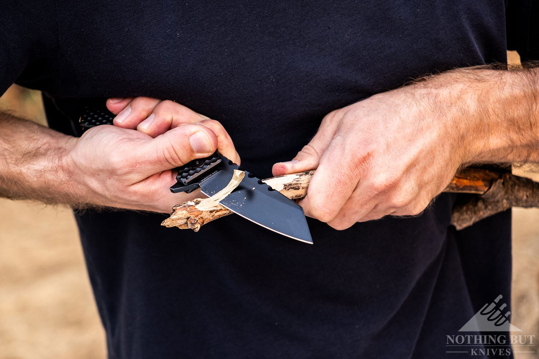 A close-up of the Off-Grid Black Mamba pocket knife being used to carve a stick using the chest lever grip, 