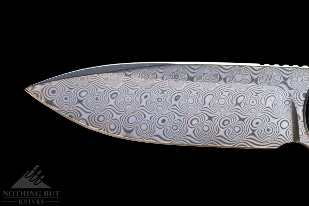 The blade of a modern Damascus steel folding knife on a black background. 