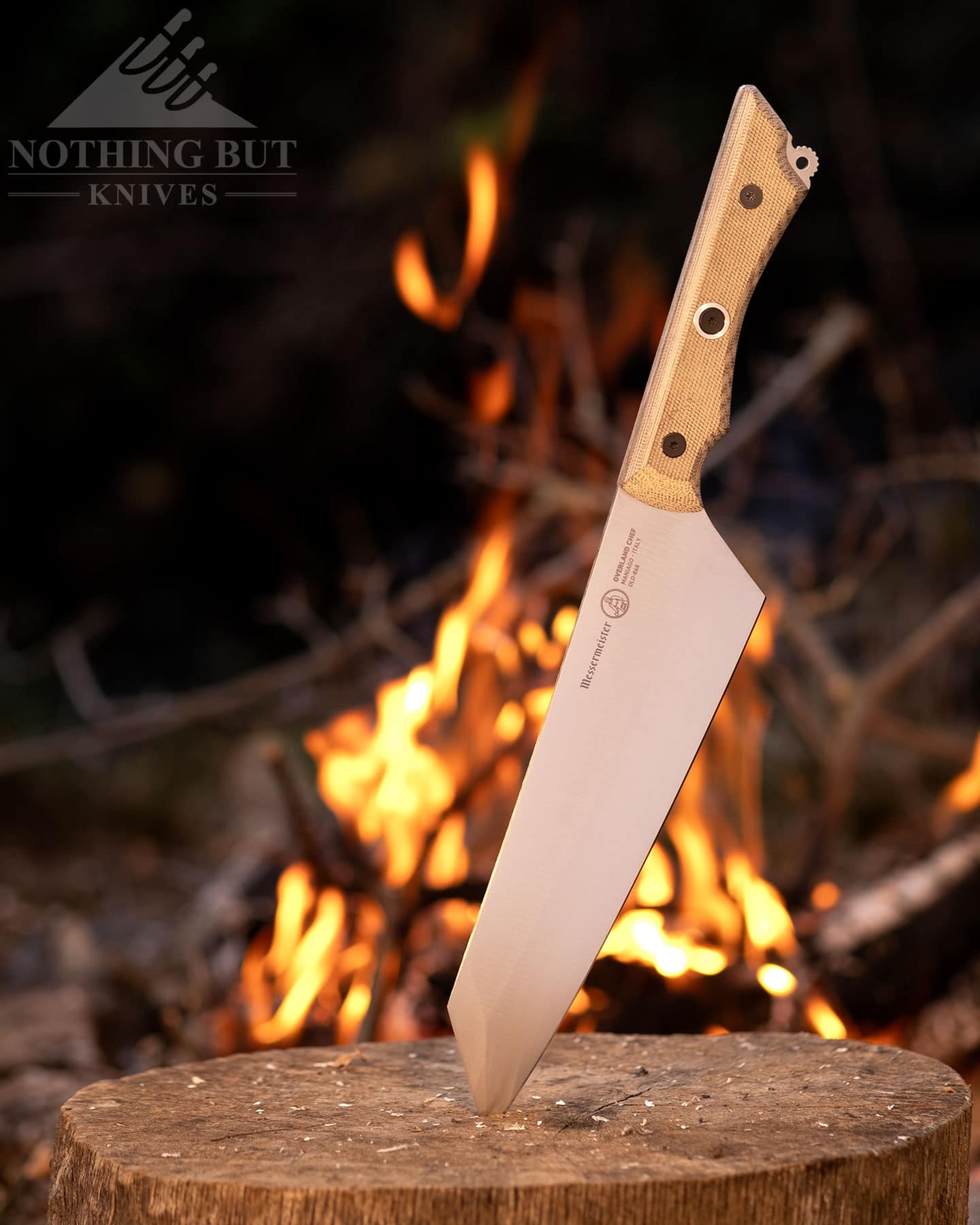 The Messermeister Overland with its blade point stuck in a tree stump in front of a campfire.