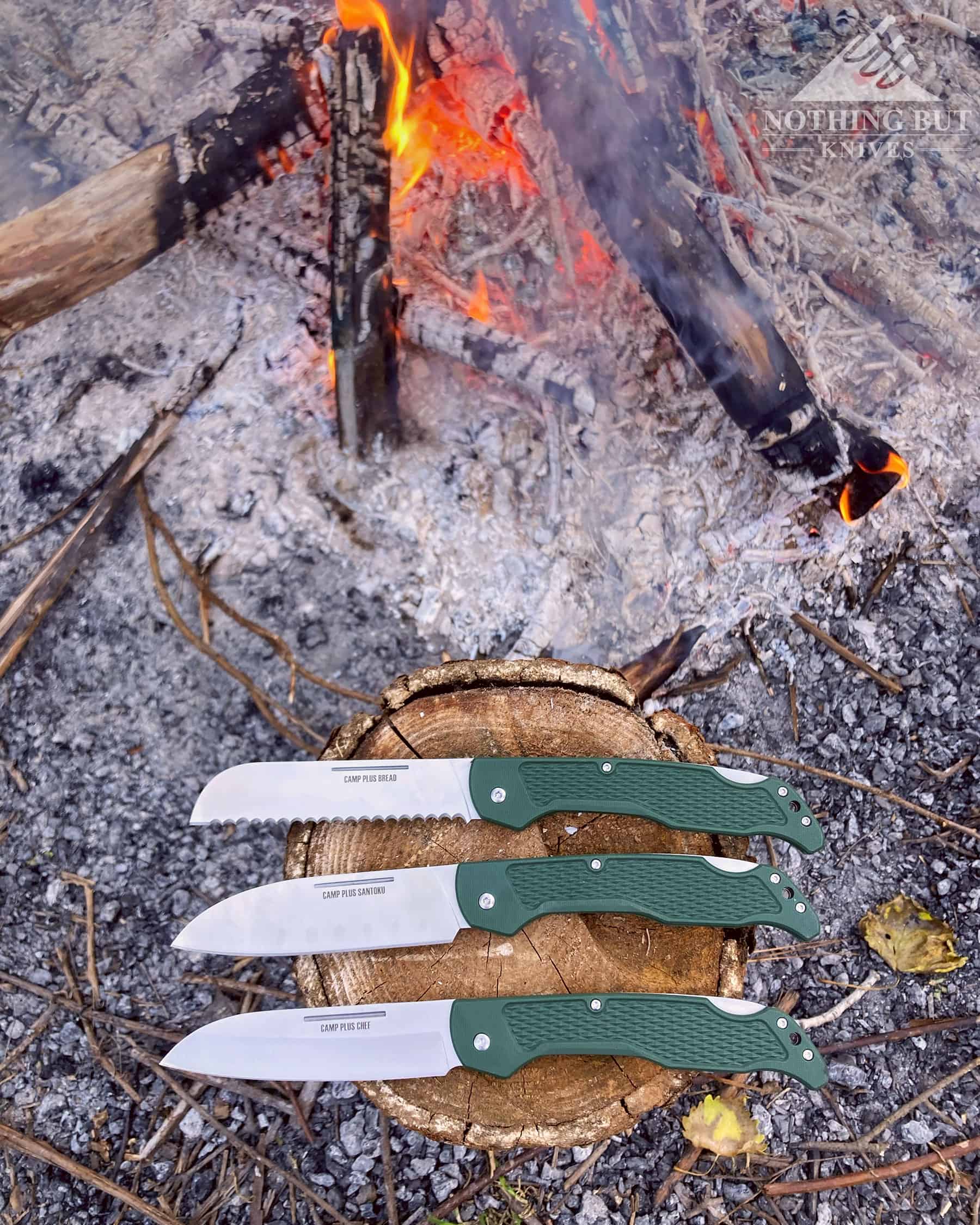 The Ontario Knife Company Camping Folders next to a campfire in the open position.