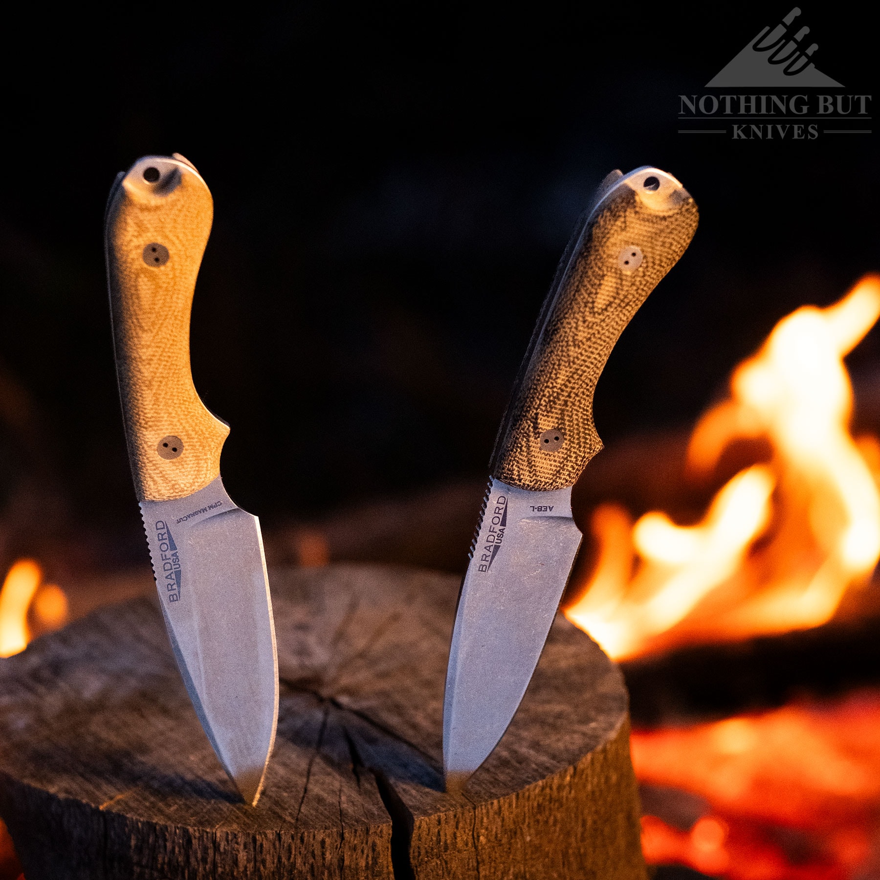 Two different versions of the Bradford Guardian 3 fixed blade knife sticking out of a piece of firewood in front of a campfire. 